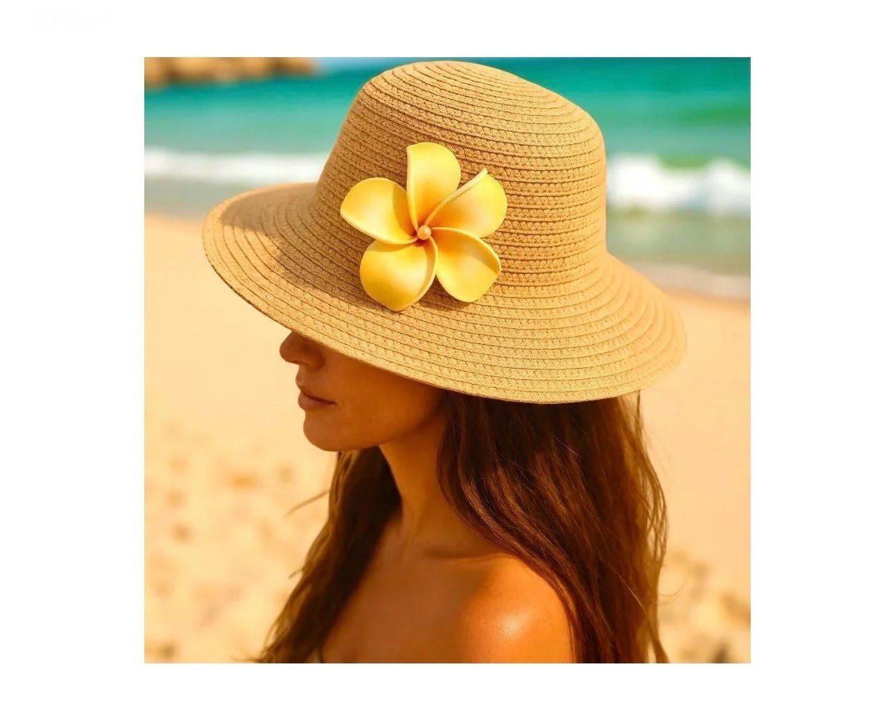 A woman wearing a wide-brimmed straw hat with a yellow flower decoration, on a beach with the ocean in the background.
