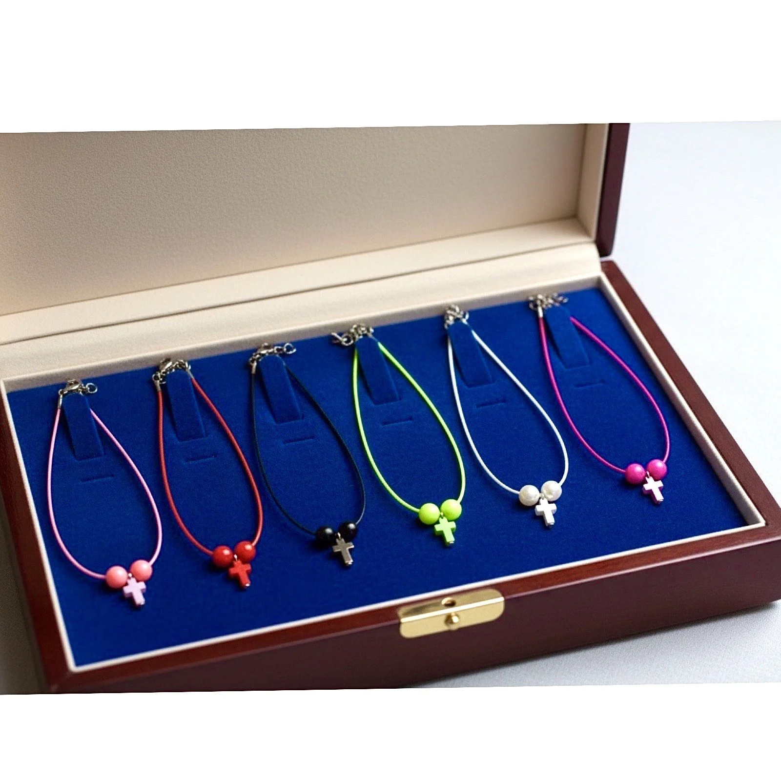 Set of five colorful necklaces with cross pendants arranged in a decorative box with a blue felt lining.