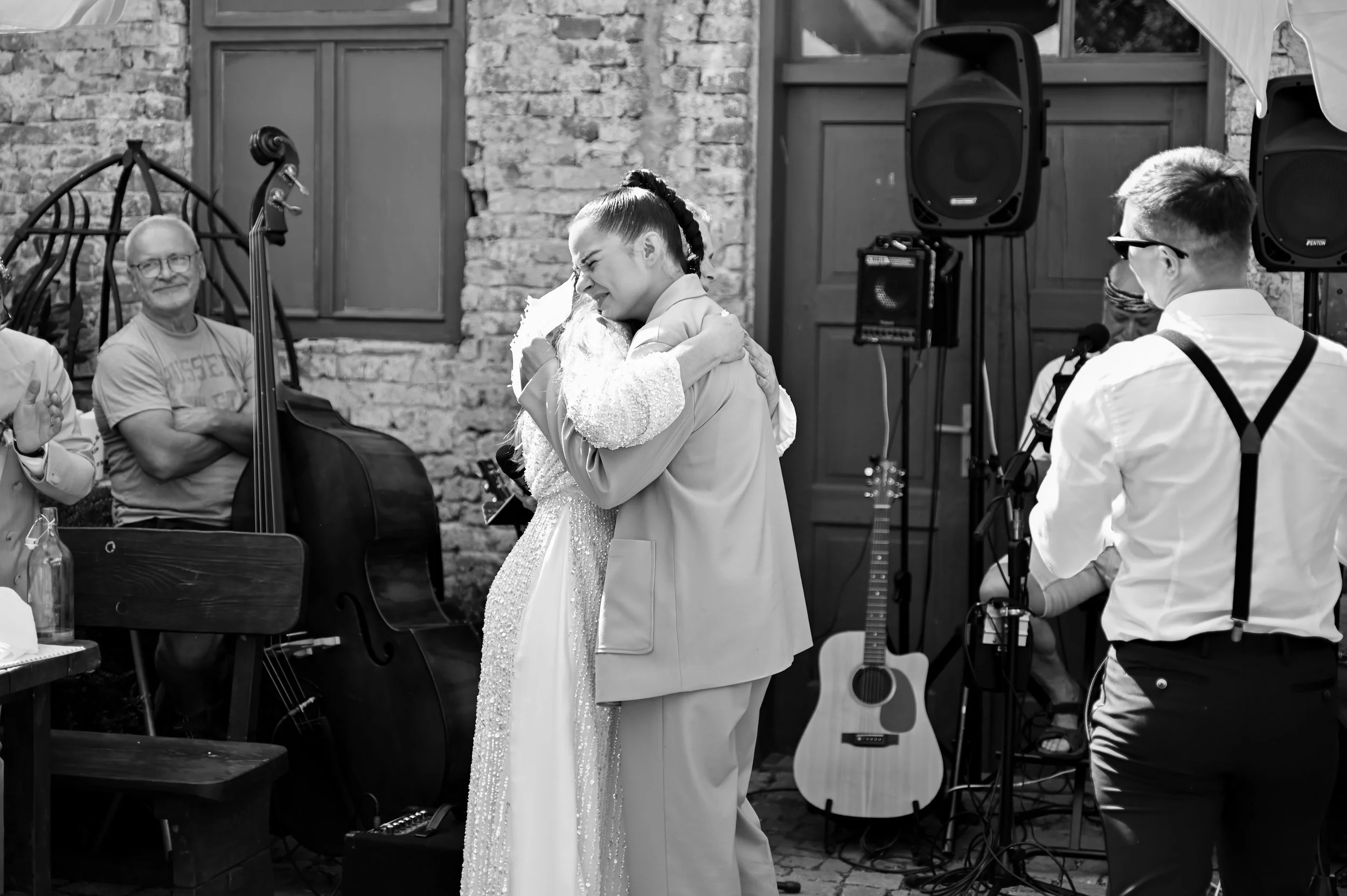A woman and a man hugging during an outdoor celebration, with a musical band and guitar in the background.