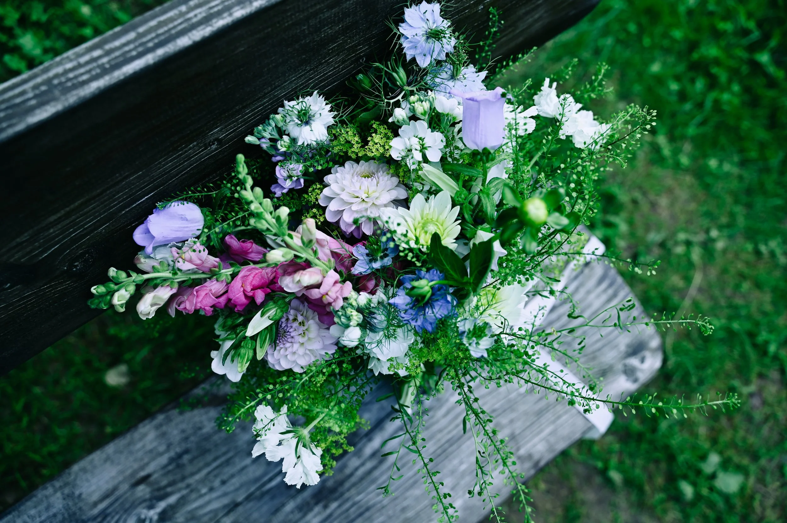A bouquet of colorful flowers resting on a wooden surface with greenery in the background.