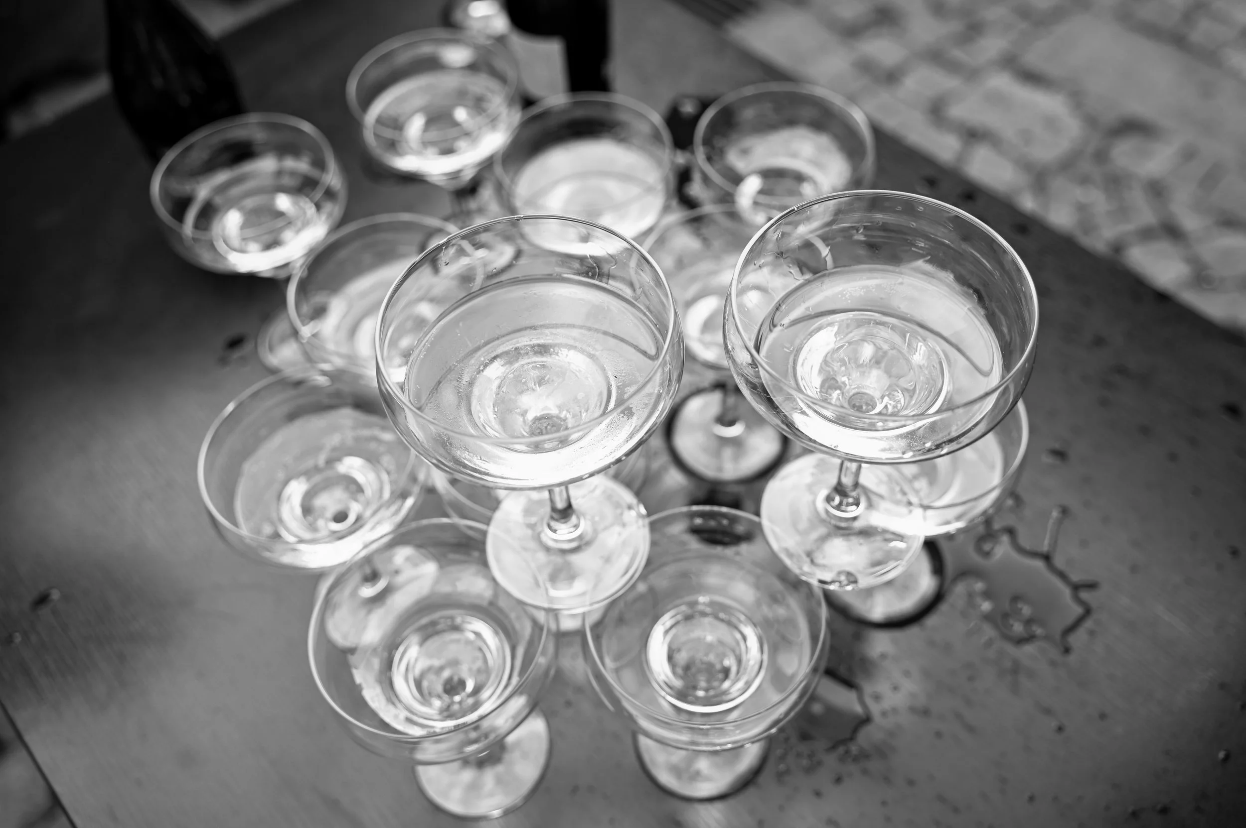 Multiple empty champagne glasses placed on a wooden surface, some filled with water, in black and white photography.
