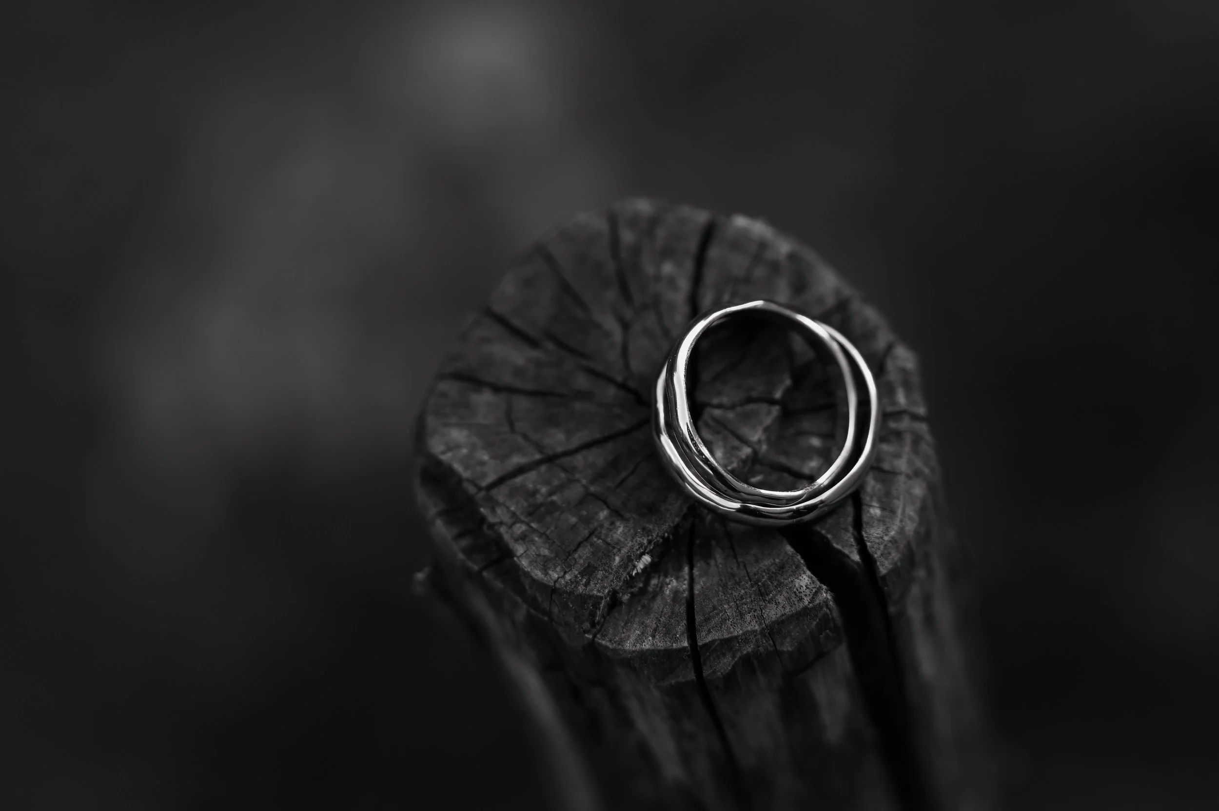 A silver ring resting on a weathered, cracked log in black and white.