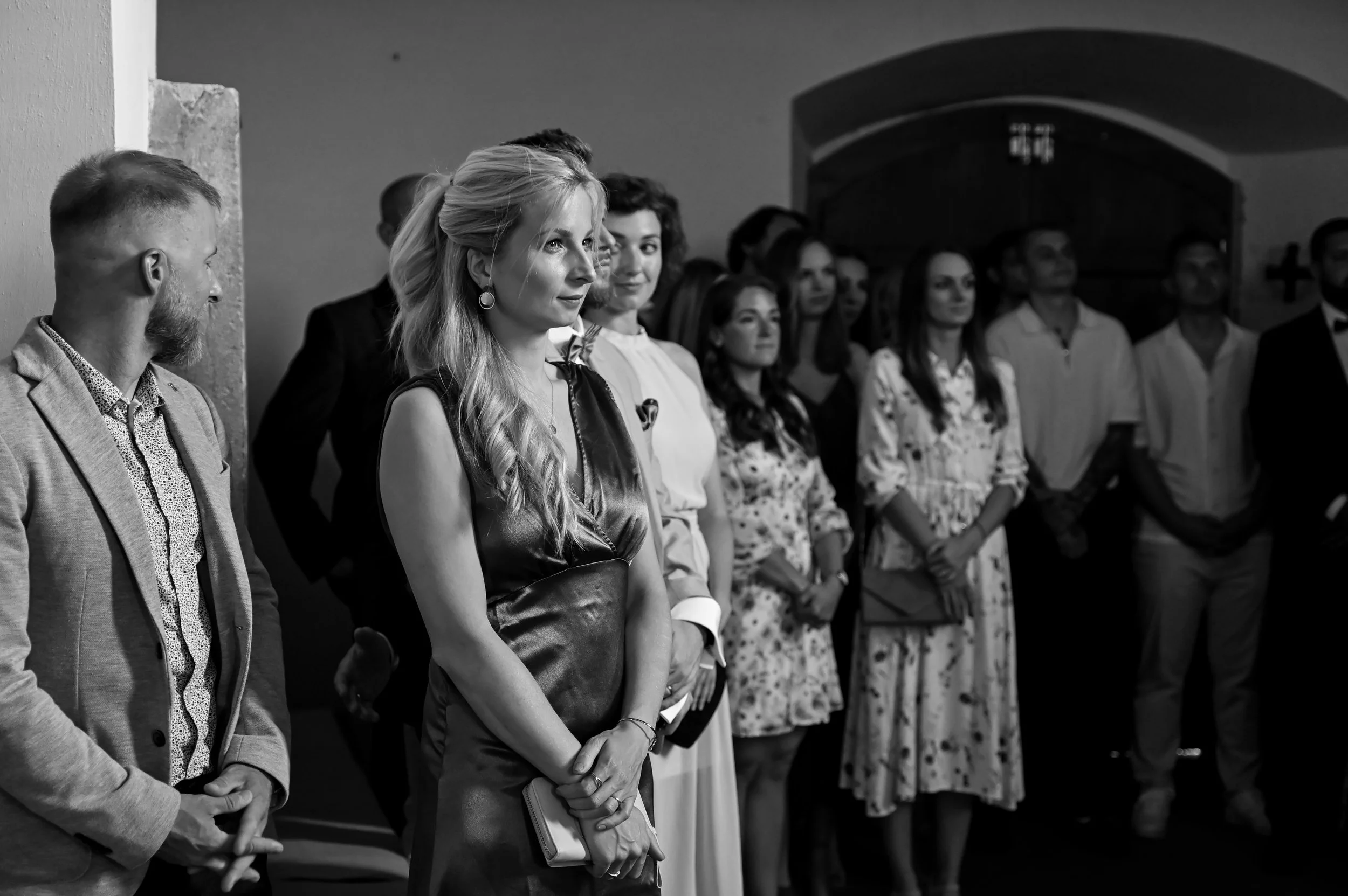 A group of people dressed in formal attire standing inside a room, attending a ceremony or event.