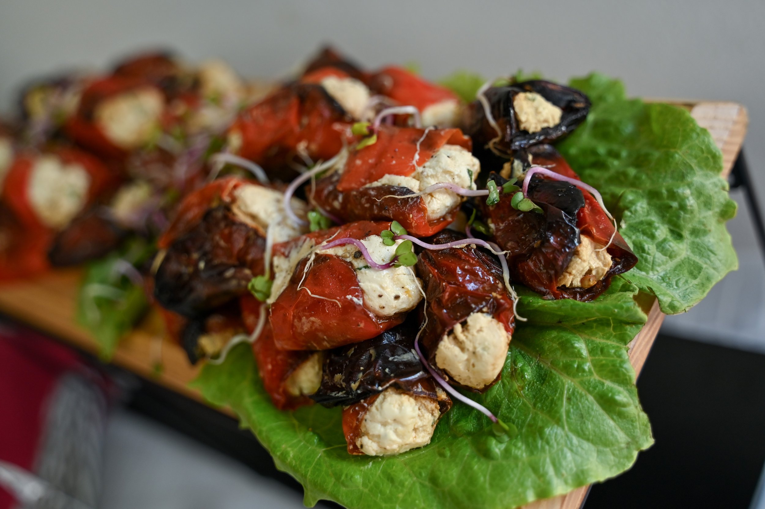 Stuffed roasted peppers with cheese and microgreens on a bed of leafy lettuce.