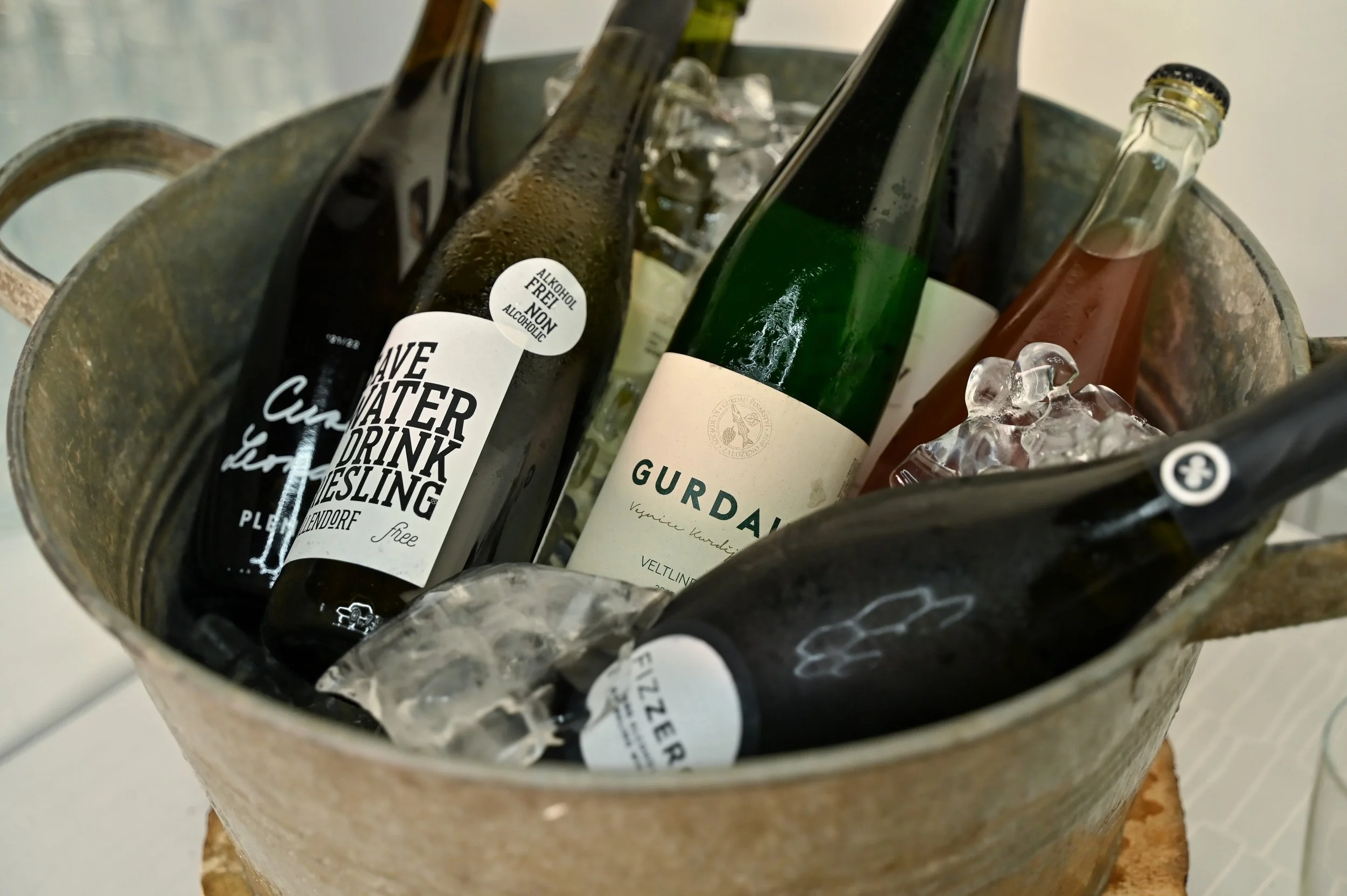 Assorted bottles of alcoholic beverages, including beer and wine, in an ice bucket with ice cubes.