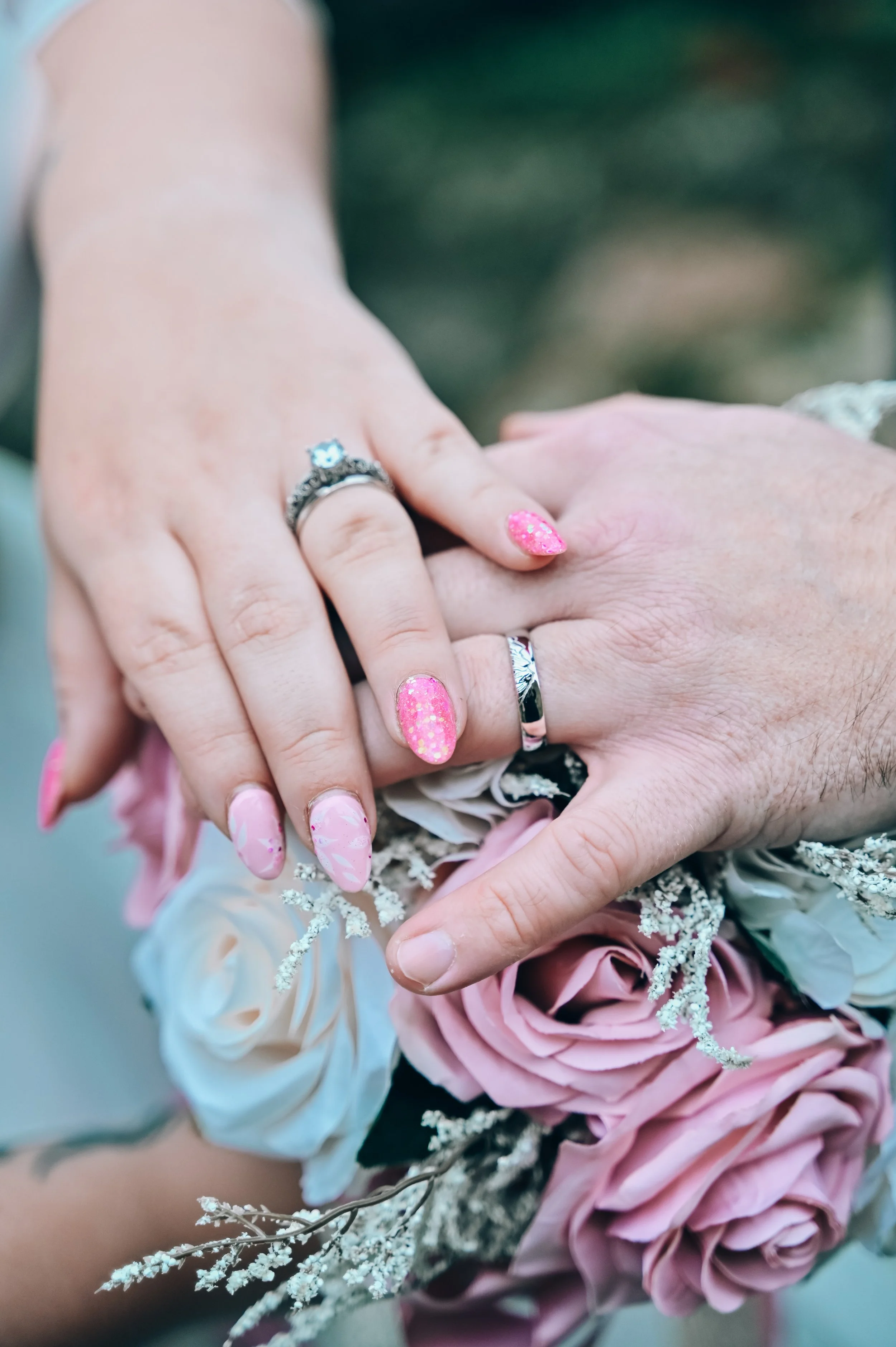 Close-up of a man and woman showing their wedding rings with a bouquet of pink and white roses.