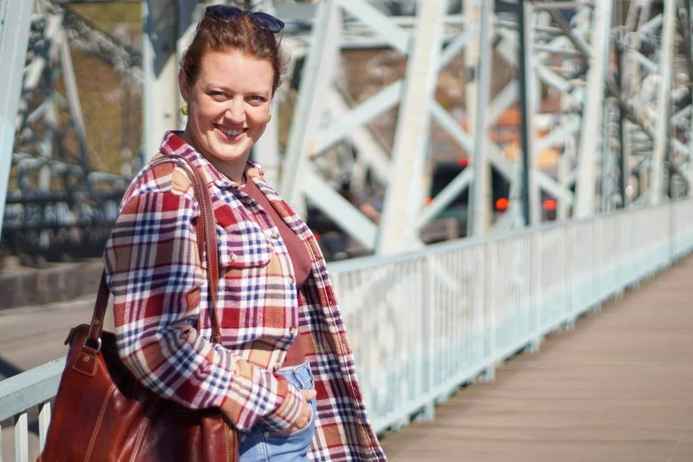 Eine Frau steht auf einer Brücke mit Eisenkonstruktion und lächelt in die Kamera.