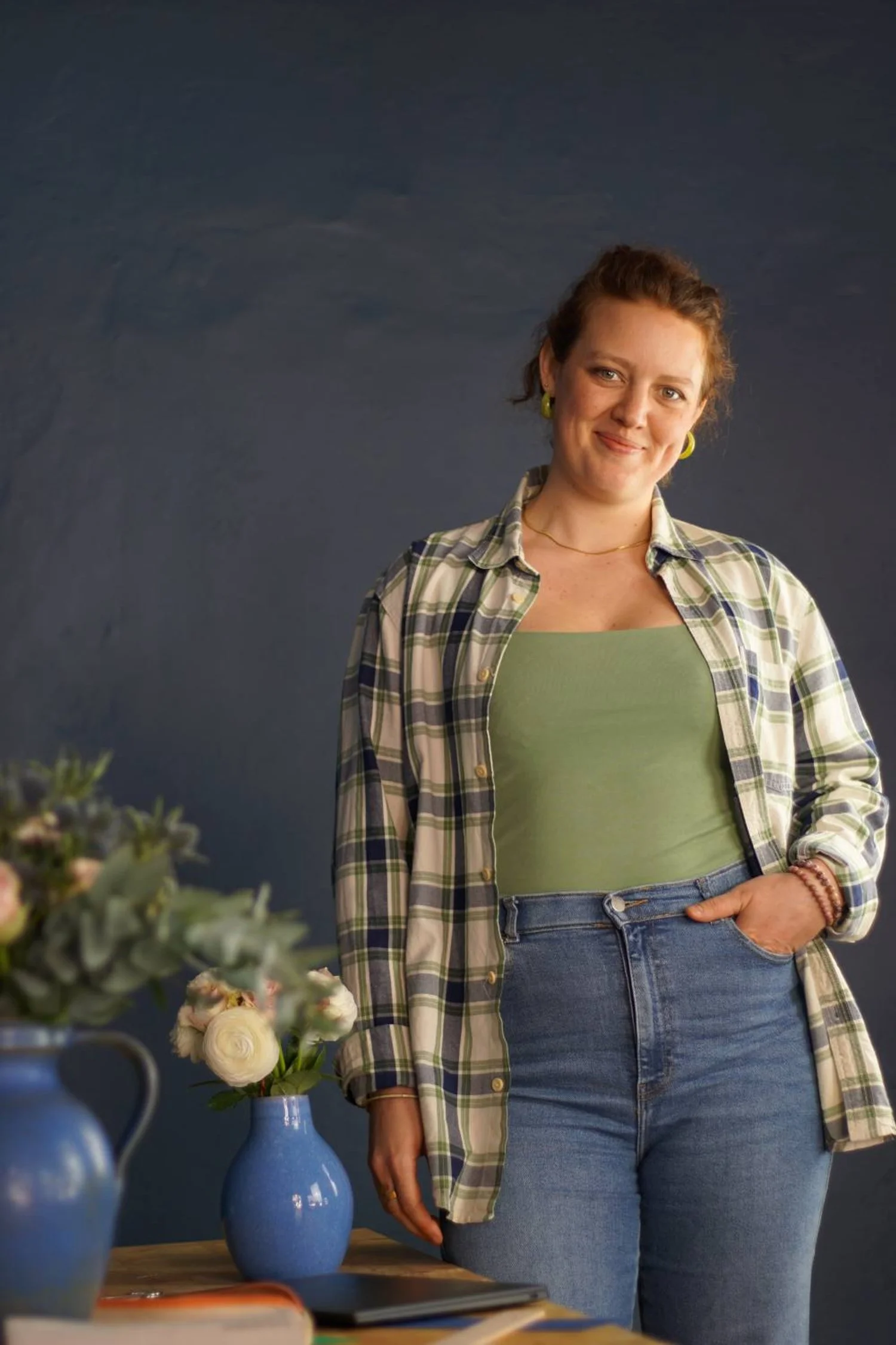 Frau steht neben lächelnd neben einem Schreibtisch, auf dem Arbeitsmaterialien und Blumensträuße stehen.