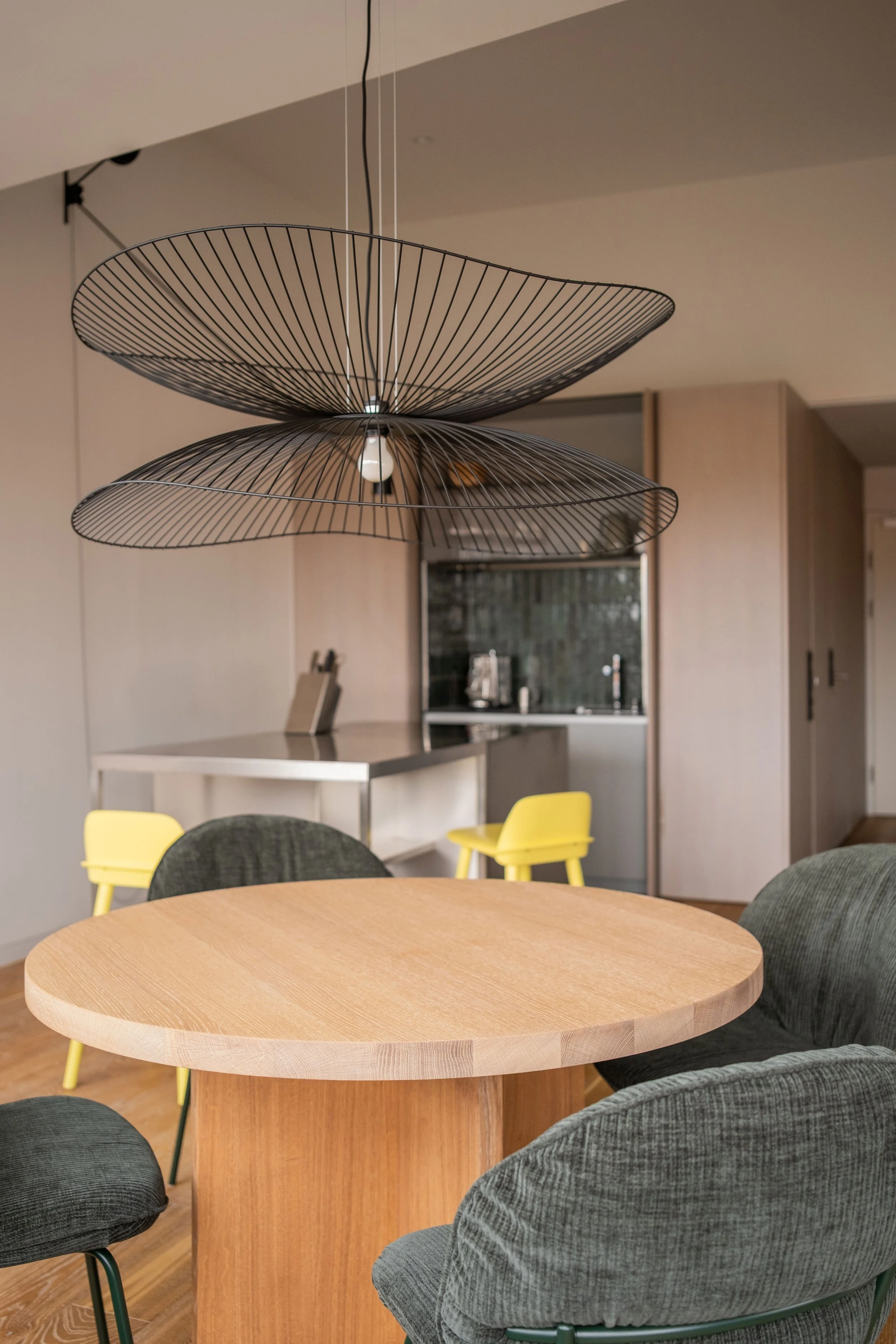 Runder Holz Esstisch in einem modernen Esszimmer, umgeben von grünen Stühlen, mit einer Deckenleuchte aus Metall in Blattform.