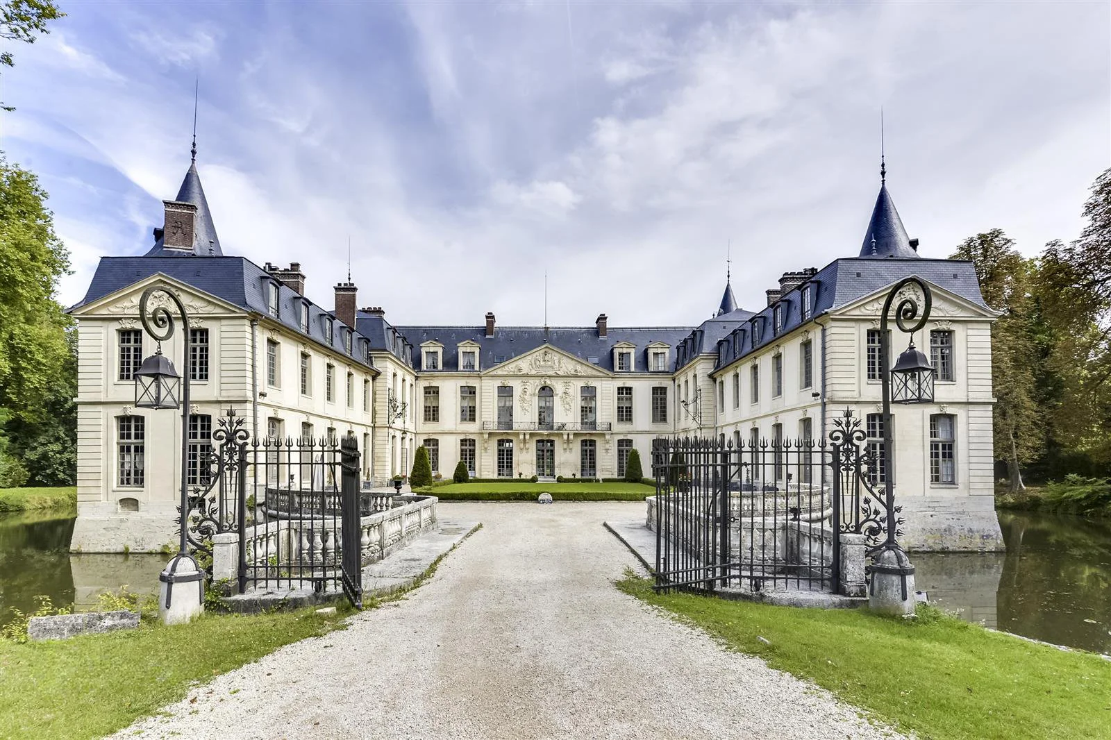 Le Château Ermenonville, monument historique avec le toit mansardé, entouré de jardins, un chemin central et un portail en fer forgé.