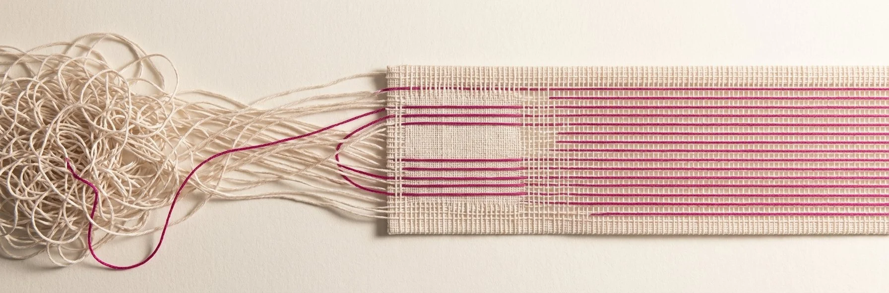 A continuous piece of thread-work running left to right, from a chaotic pale tangle into ordered woven cloth with magenta threads running straight and parallel.