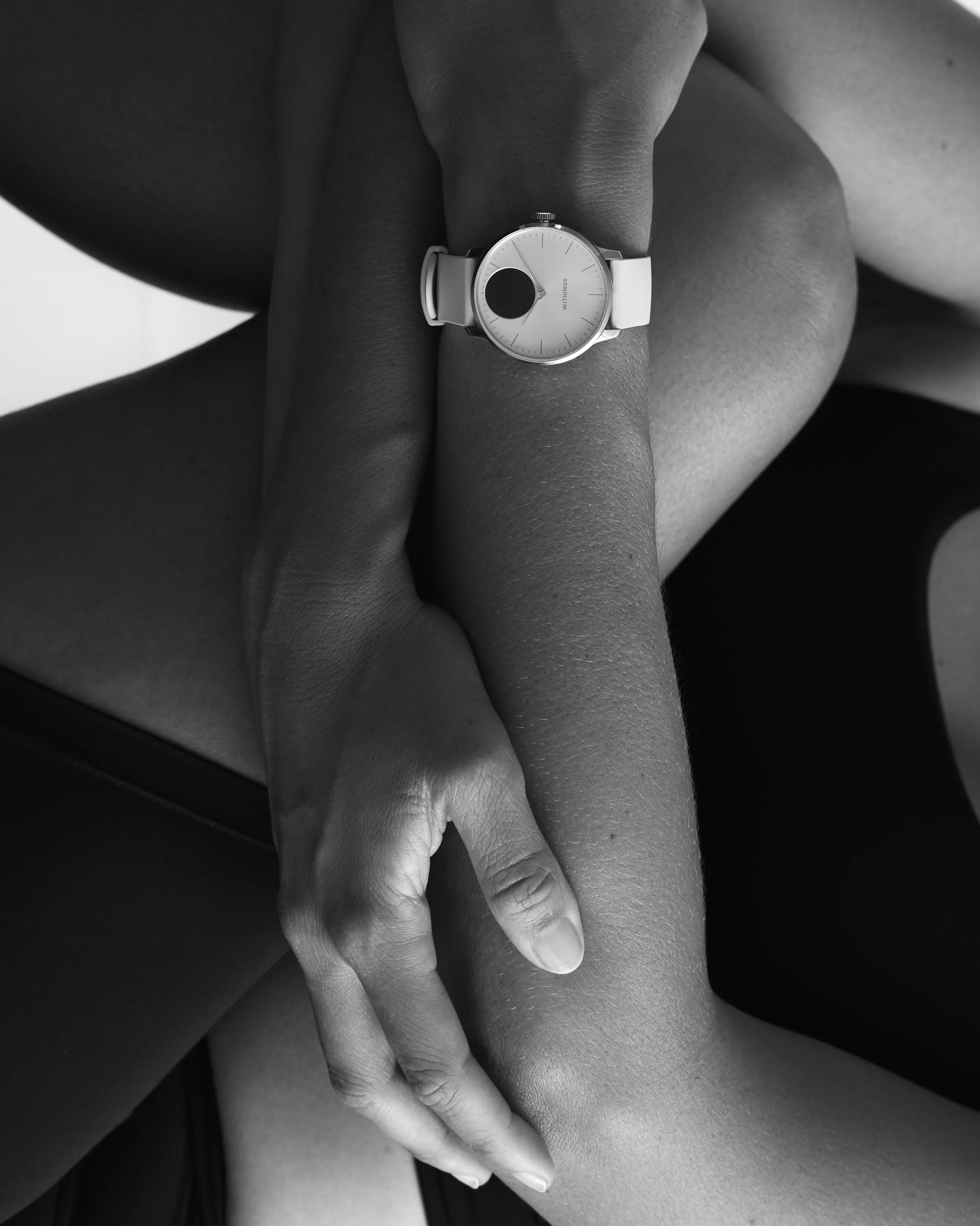 Close-up of two hands gently holding each other, one hand wearing a wristwatch, in black and white.