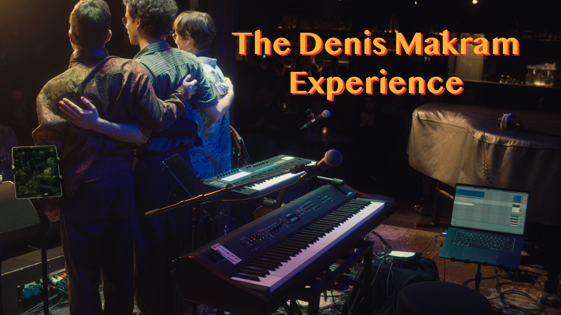 Band members on stage with keyboards and microphones, "The Denis Makram Experience" text.