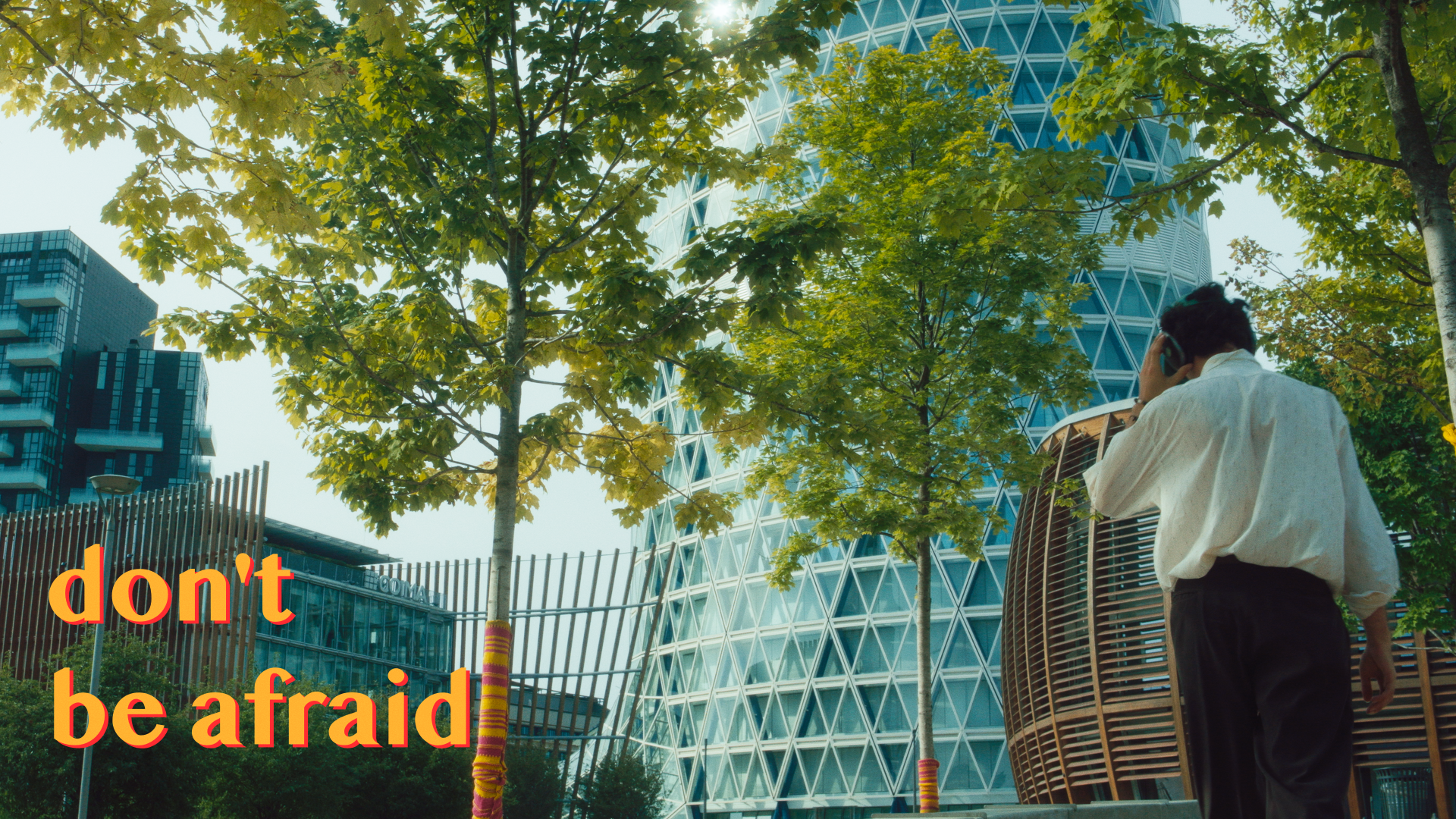 Urban scene with modern buildings, trees, and a person talking on a phone. Text "don't be afraid" appears in the foreground.