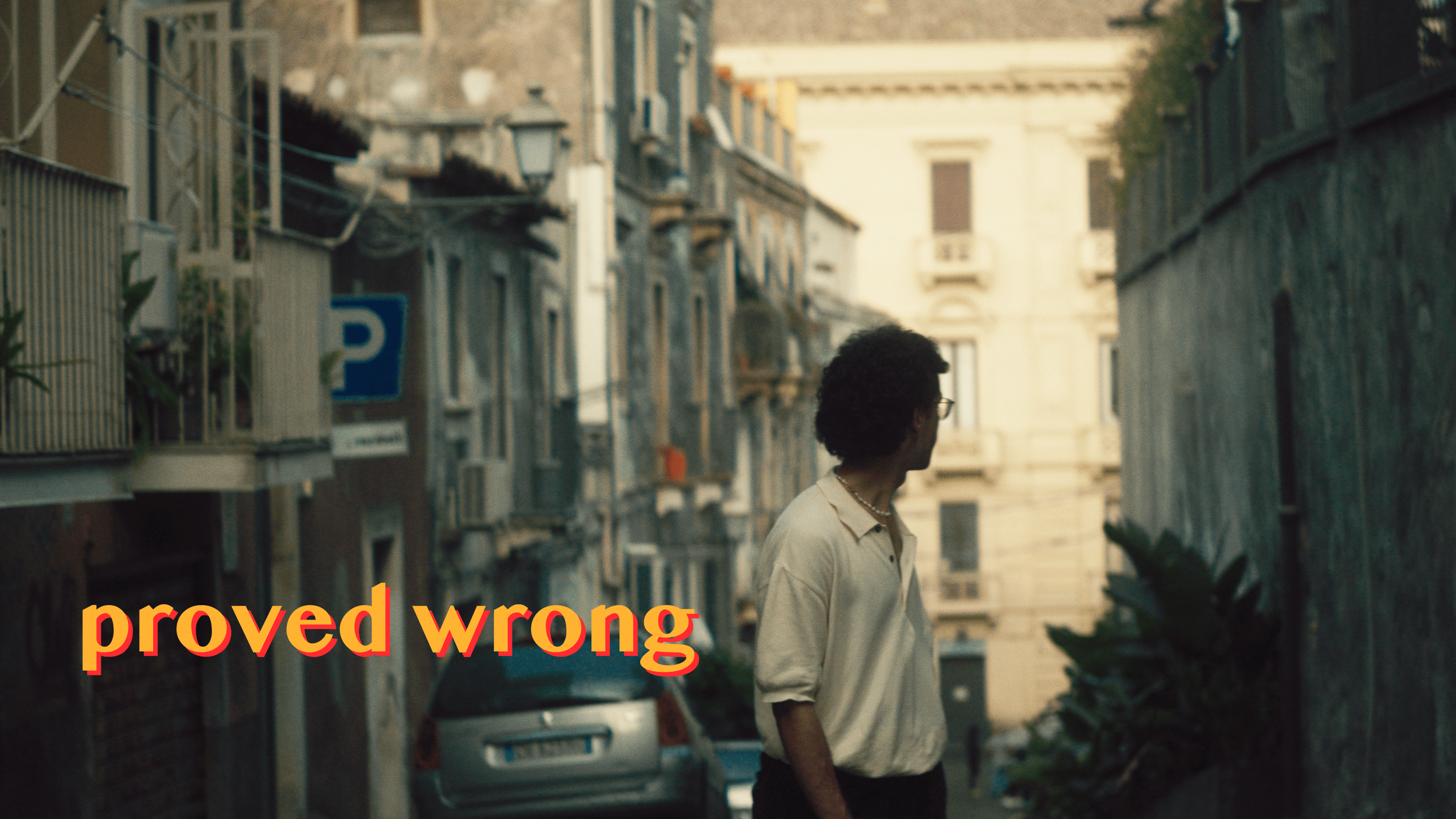 Person standing on a narrow street with European architecture in the background, viewed from behind. The text "proved wrong" is overlaid on the image.