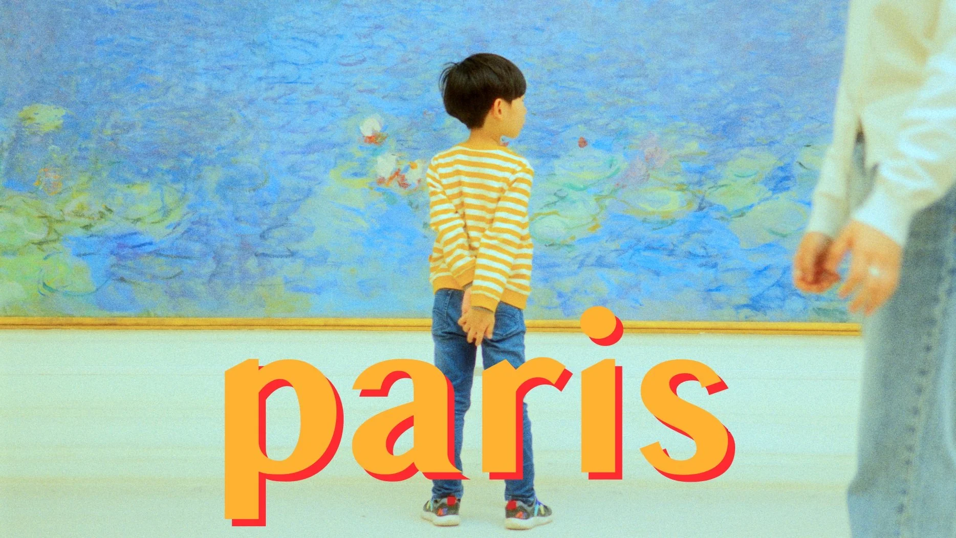 Child in striped shirt standing in front of a large blue and green painting in a gallery setting with the word 'paris' in bold yellow text overlay.