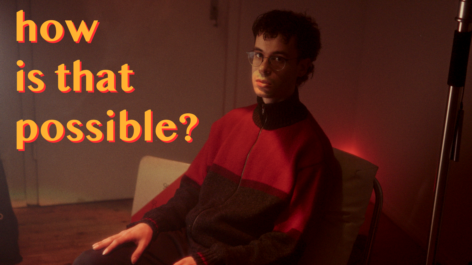 Person in a dimly lit room wearing a red and black sweater, seated on a chair, with text "how is that possible?" in bold yellow letters.