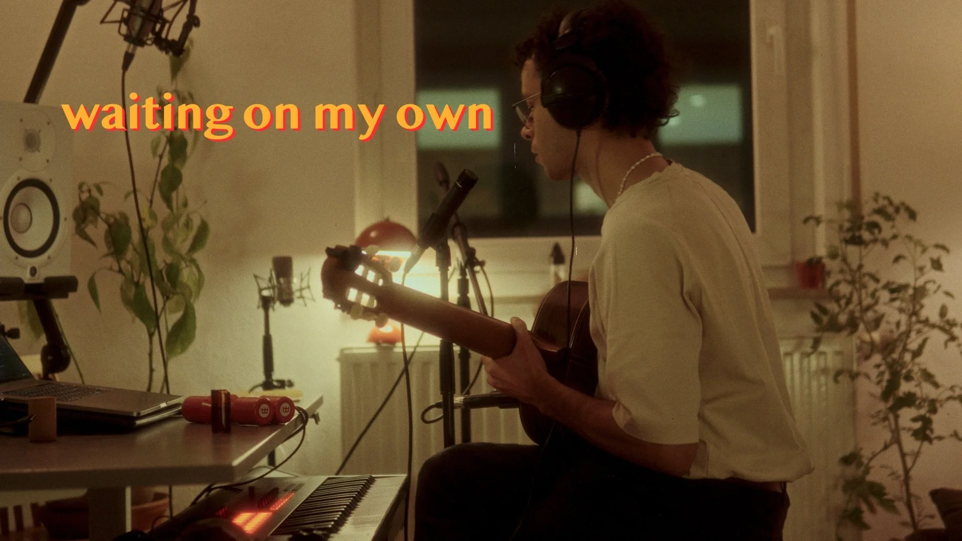 Person playing guitar in a room with recording equipment and the text "waiting on my own" in the background.
