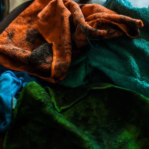 Pile of hazardous waste oily cloths and mechanical rags, including orange, blue, green, and teal, in various textures and conditions.