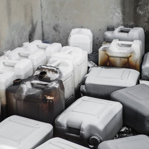 Plastic hazardous waste jerry cans in a corner, some stained and worn.