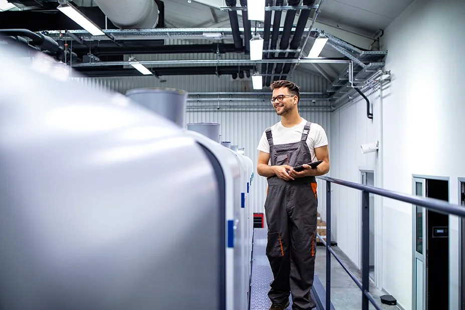 Engineer wearing reading glasses and grey overalls using TAG Mobi on a tablet to monitor a manufacturing facility performance for preventive maintenance and asset management.