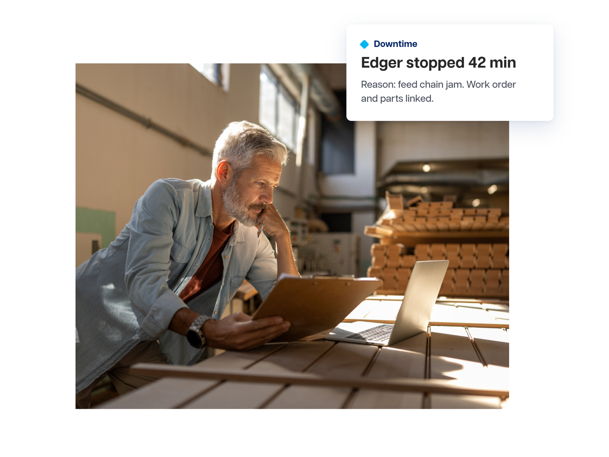 A mill supervisor reviews a clipboard and laptop beside stacked lumber in a sawmill, with a card showing a downtime event.