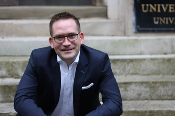Dr Stuart Robb, in a suit sitting on stone steps.