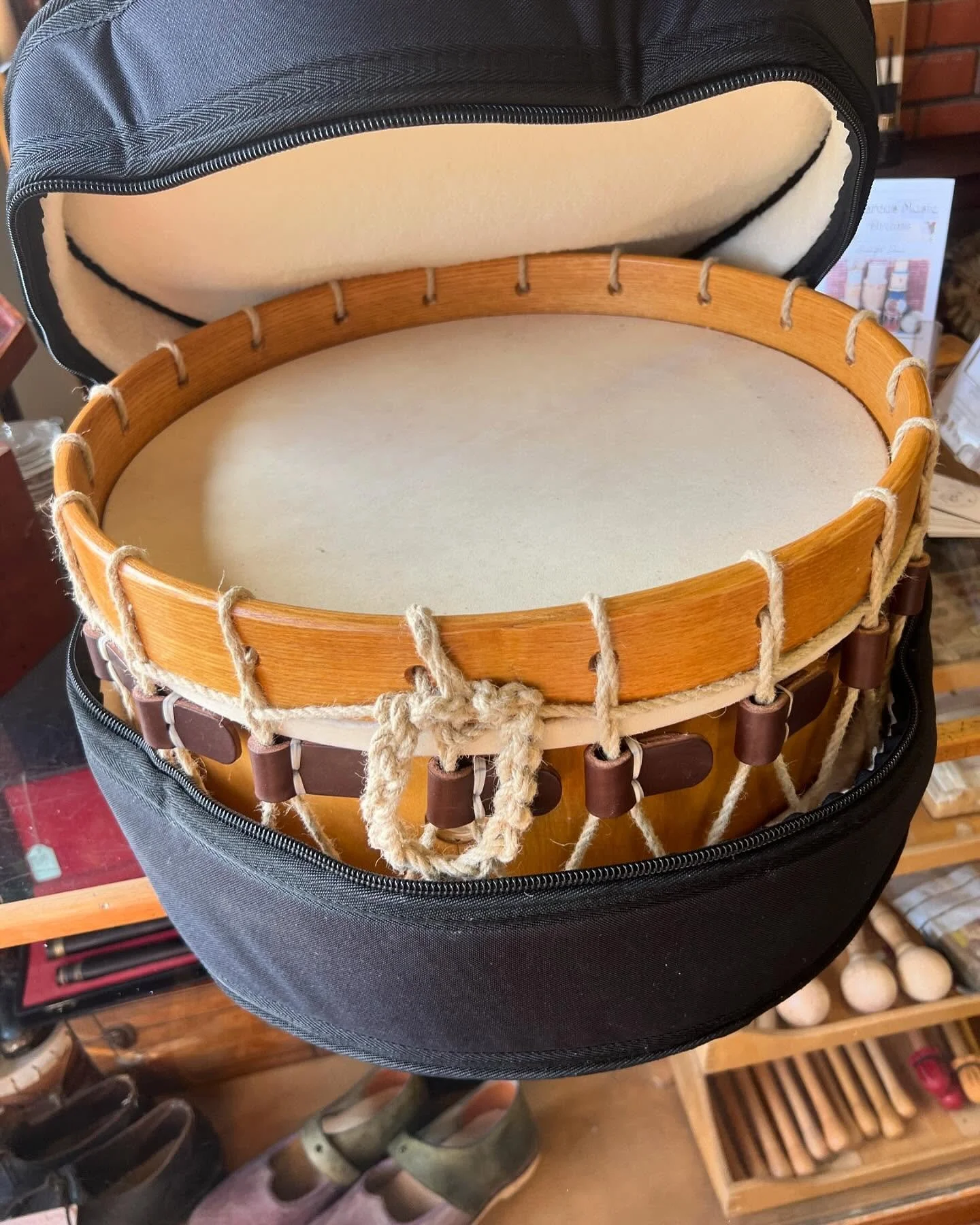 A wooden frame drum inside an open black case, showing the drumhead and rope tensioning system.