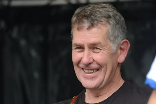 Ywain Myfyr, smiling with a blurred dark background.