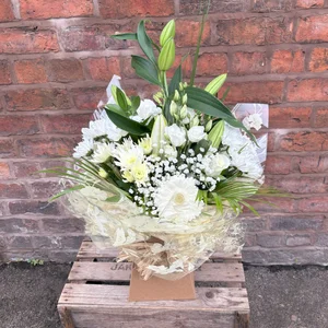 White floral aqua pack bouquet with lilies, roses, and greenery with a decorative wrapping, placed on a wooden crate against a brick wall, made by a florist in Crewe 'Personal Flowers'.