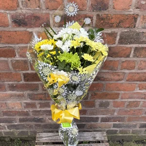 Bouquet of yellow and white flowers in decorative clear wrapping on a wooden box, set against a red brick wall background, made by a flower shop in Crewe 'Personal Flowers'.