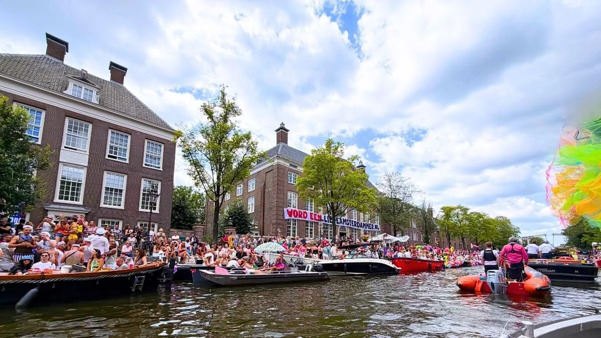 Boats traveling along the Amsterdam Canal Parade route with crowds watching from the canal banks