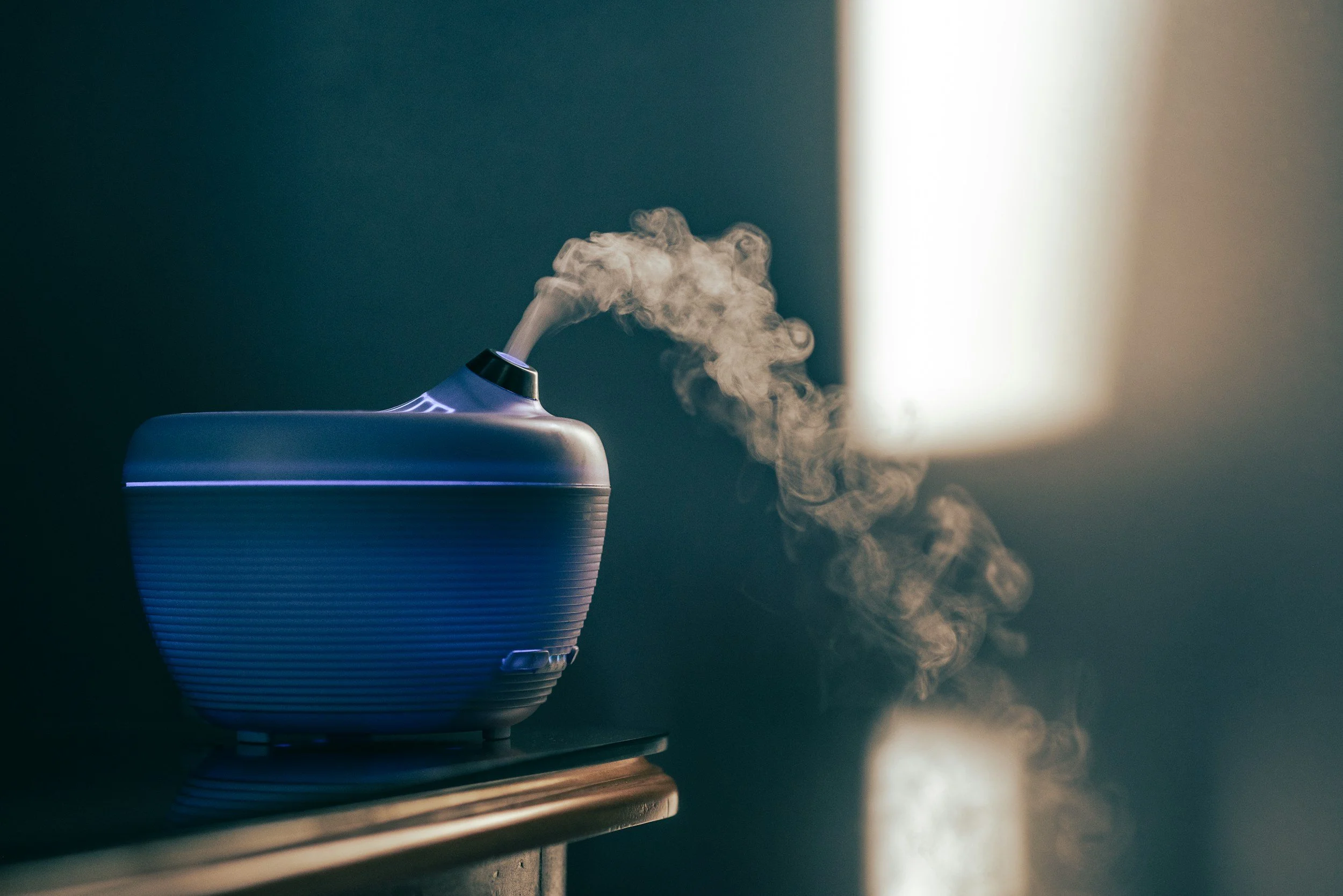 A modern diffuser emitting vapor on a dark surface with a gradient background, illuminated by a soft light.