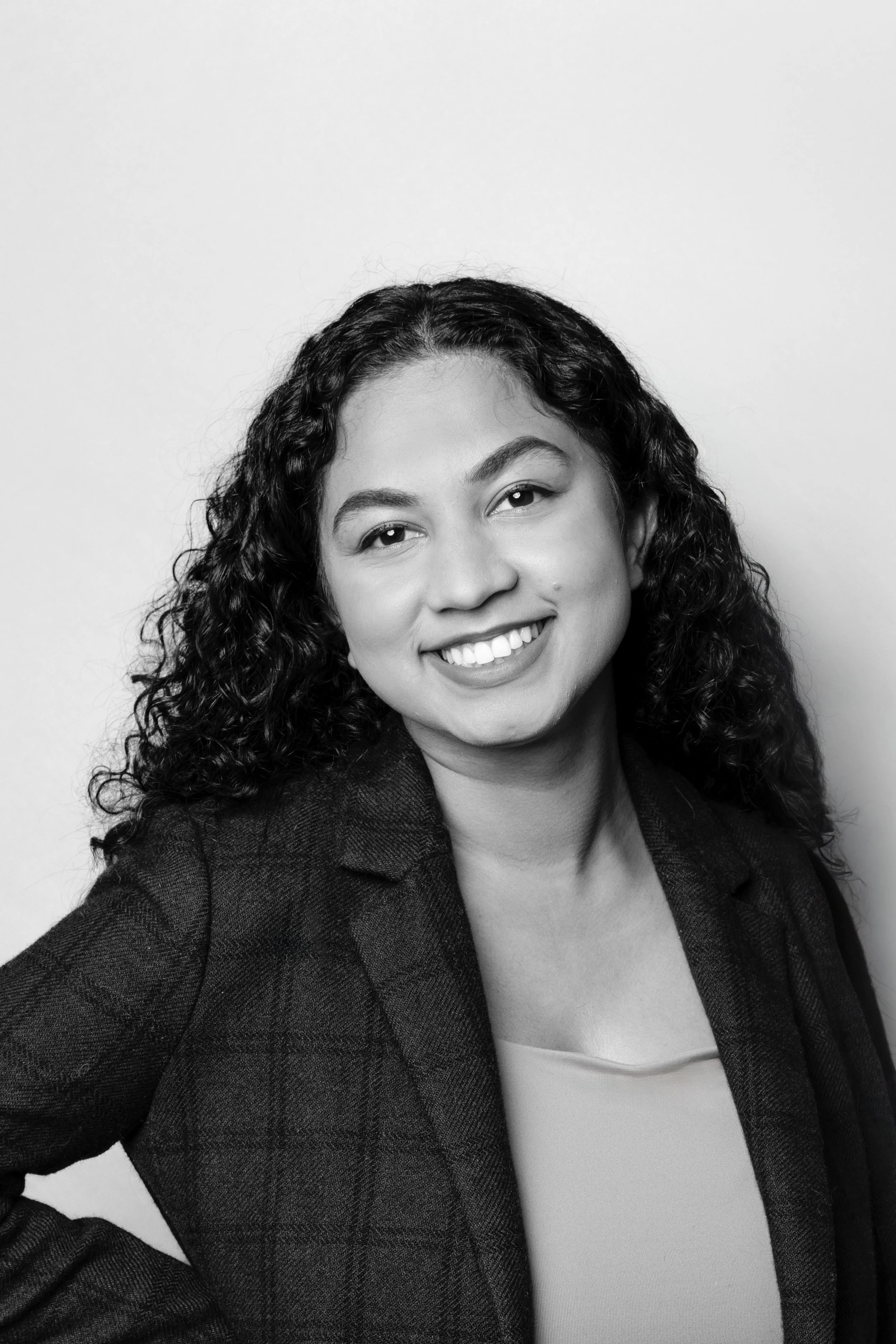 Black and white portrait of a woman with curly hair, smiling, wearing a blazer and light top, against a plain background.