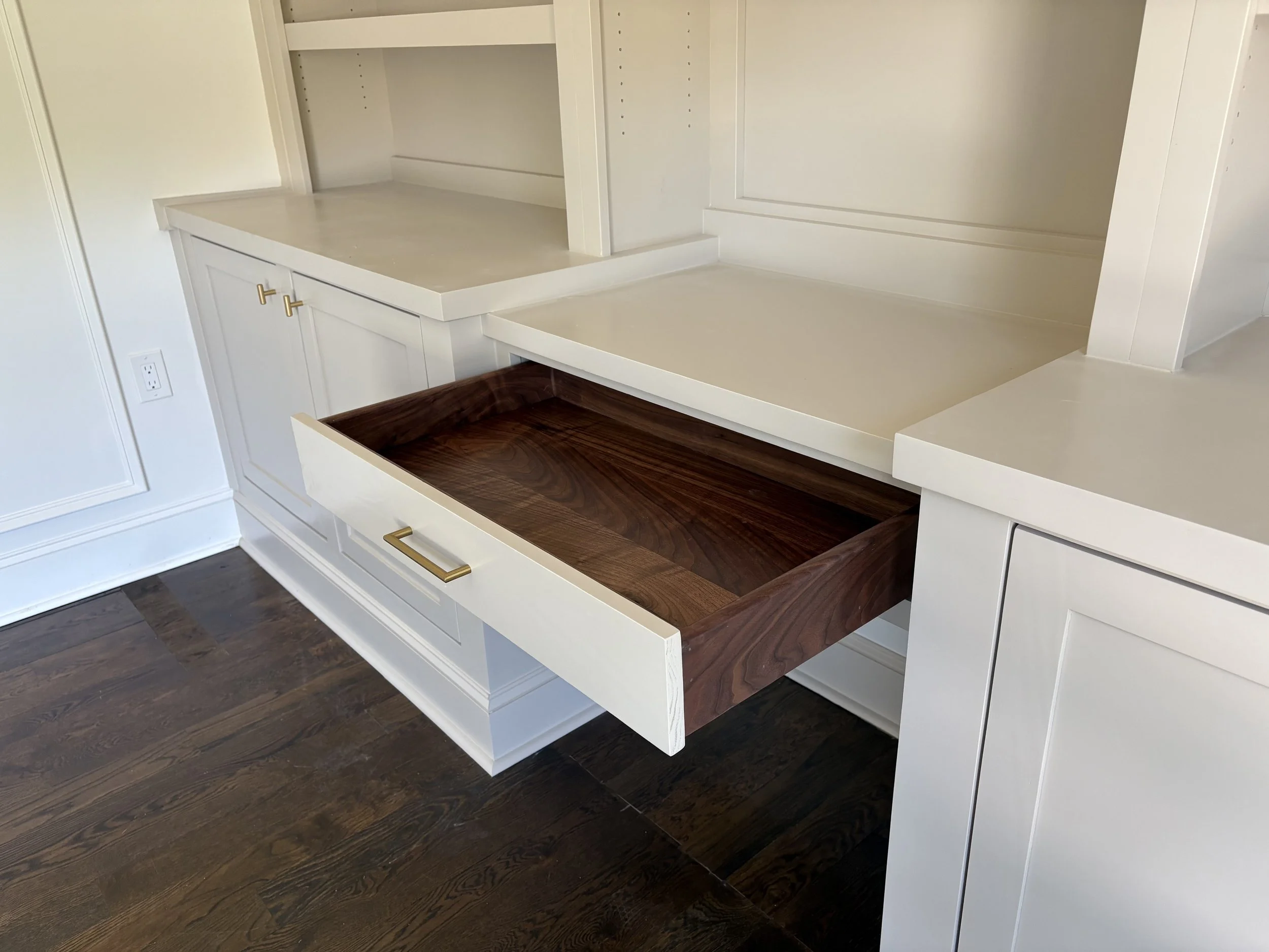 Open drawer in white cabinetry revealing a dark wood interior, with other drawers and countertops in the background.