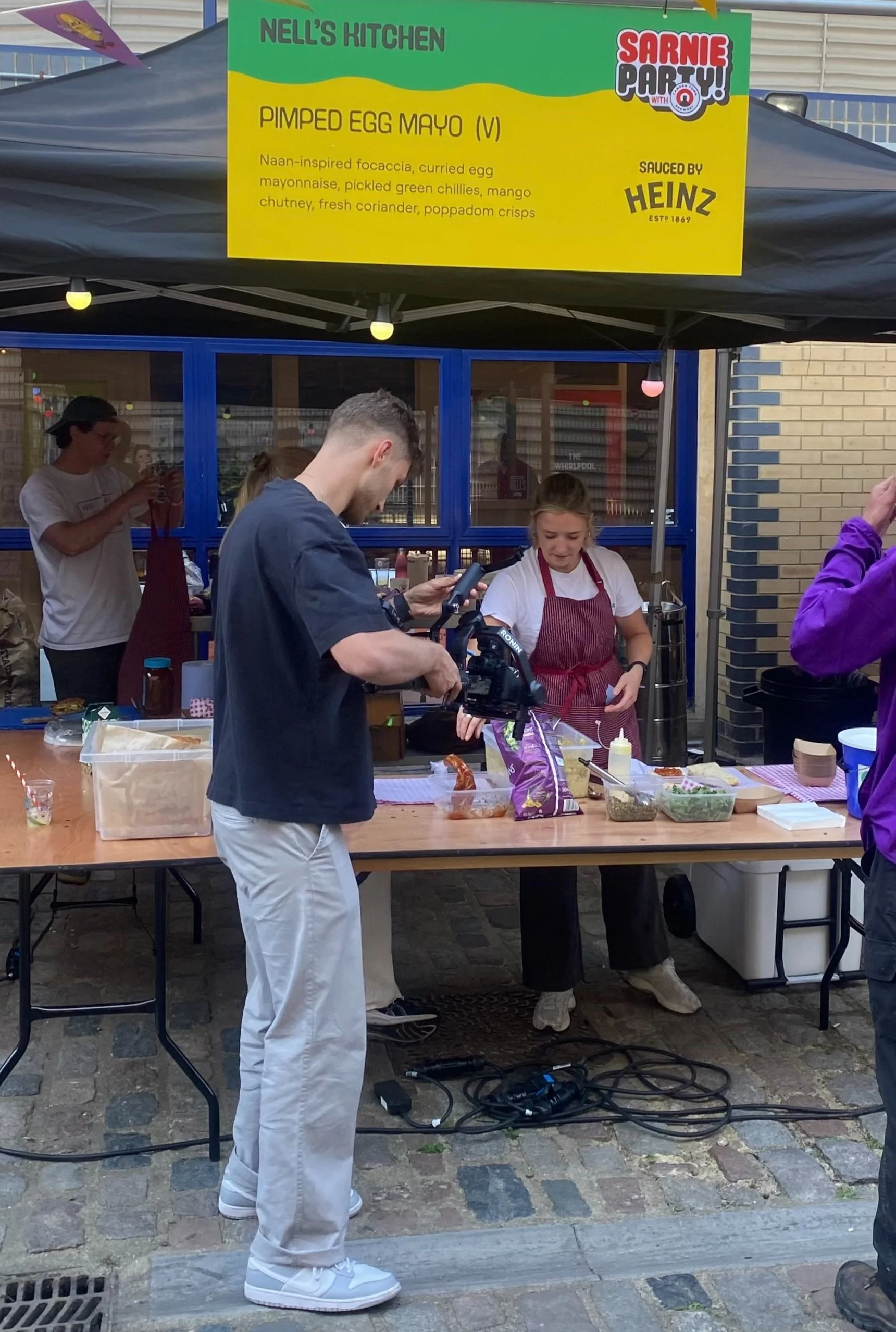 James filming a food stall vendor making sandwiches for a documentary-style video.