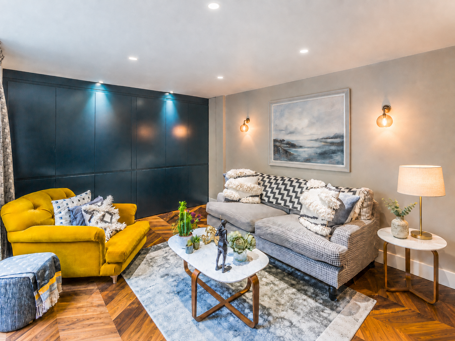 Small apartment living room seating area with mustard velvet armchair, patterned sofa and dark panelled storage wall