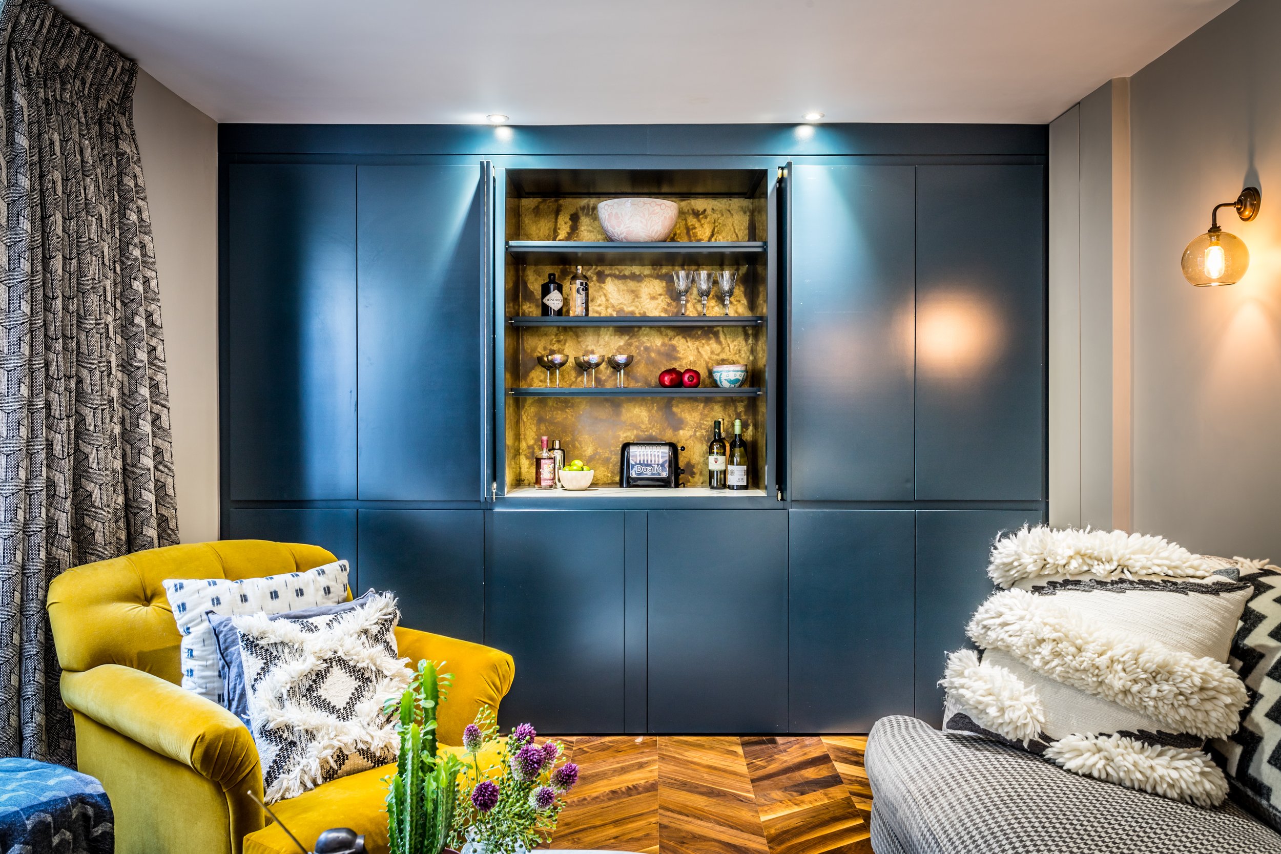 Hidden drinks cabinet built into dark blue joinery, a clever storage solution for small apartment living rooms
