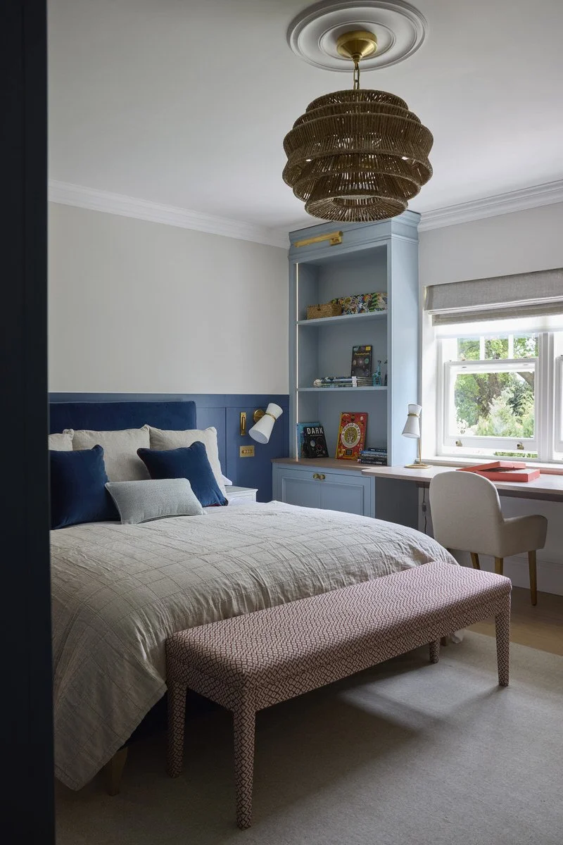 A stylish children's bedroom with a navy headboard, duck-egg blue built in shelving and desk looking out over the garden with woven pendant light above.