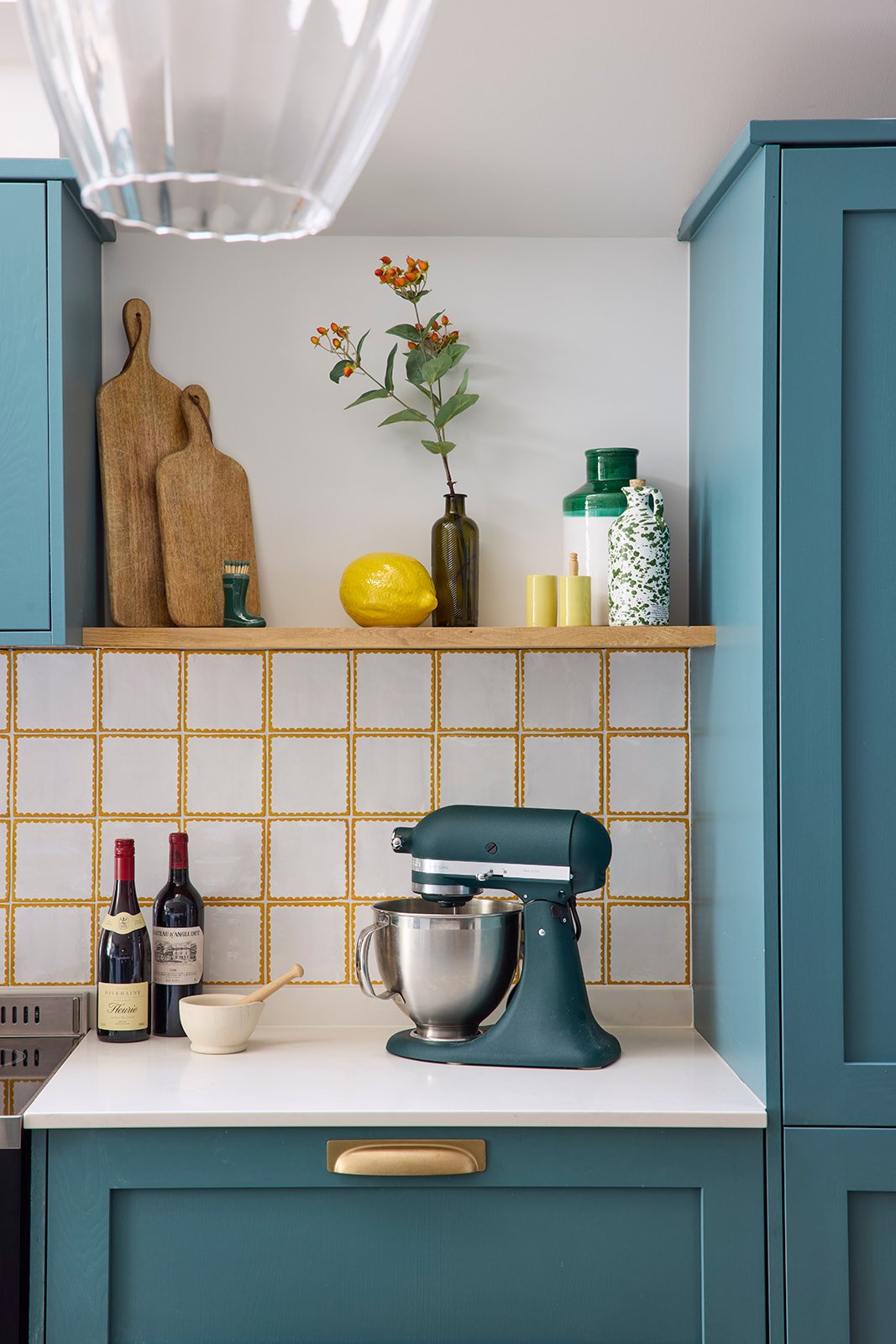 white and mustard yellow tile backsplash with wooden shelves and teal cabinets and cupboards