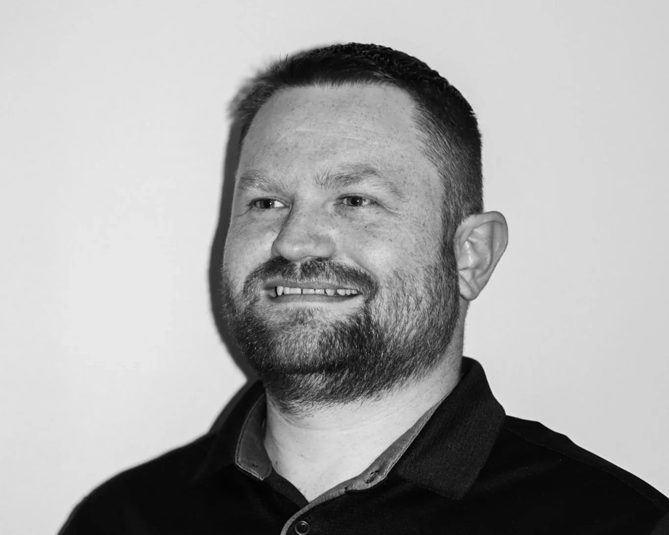 Black and white portrait of a man with short hair, beard, and missing front teeth, wearing a collared shirt, facing slightly to the left. A Connect Engineering Employee.