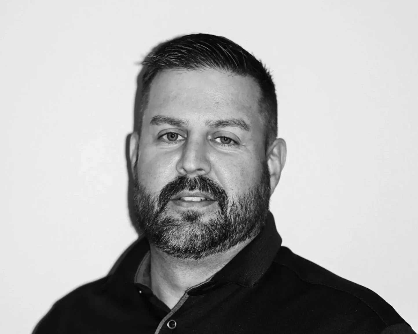 Black and white portrait of a man with short hair, beard, smiling, wearing a collared shirt, against a plain light background. A Connect Engineering Employee.
