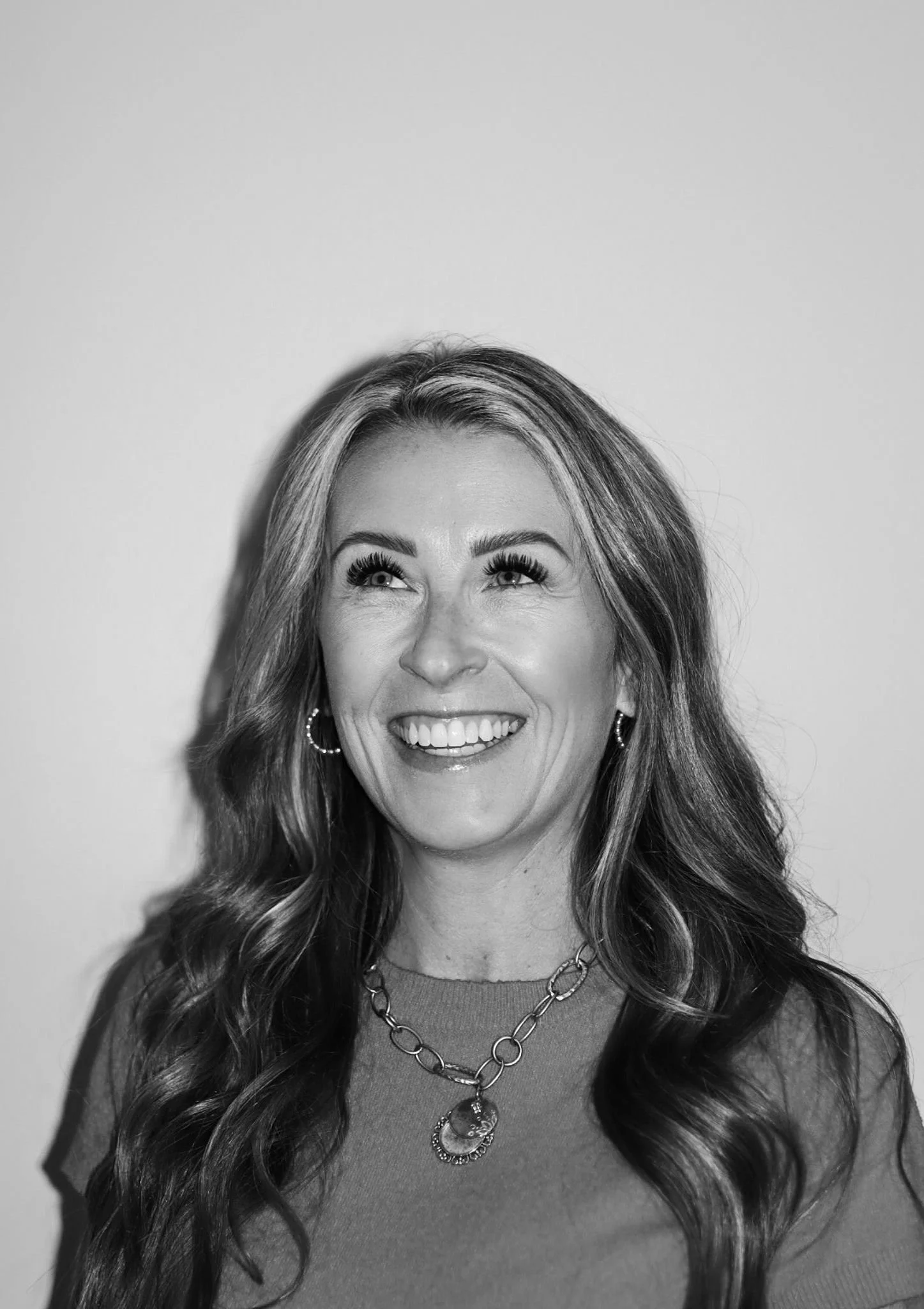 Black and white photo of a woman with long, wavy hair, smiling and looking up. A Connect Engineering Employee.