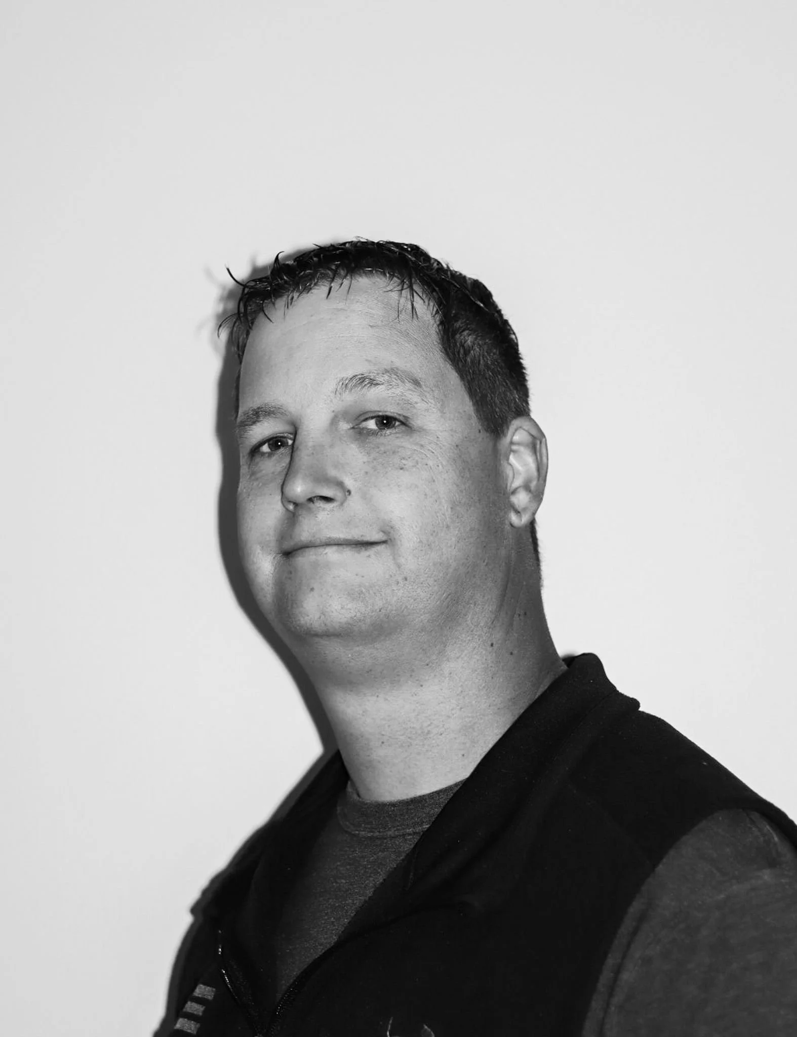 Black-and-white portrait of a man looking at the camera, wearing a dark jacket over a T-shirt, against a plain background. A Connect Engineering Employee.