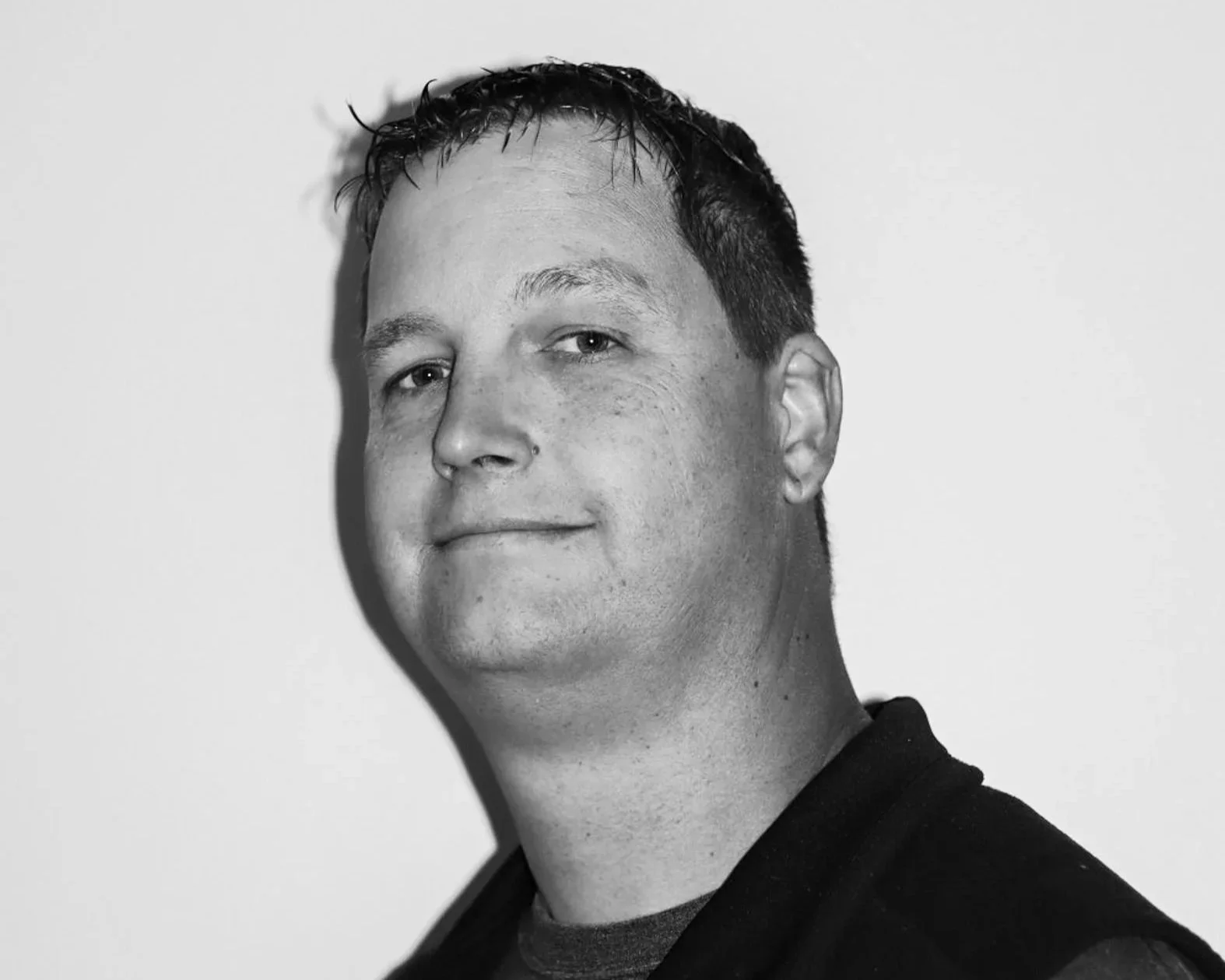 Black and white portrait of a man with short, dark hair, wearing a dark jacket over a t-shirt, smiling slightly against a plain light background. A Connect Engineering Employee.