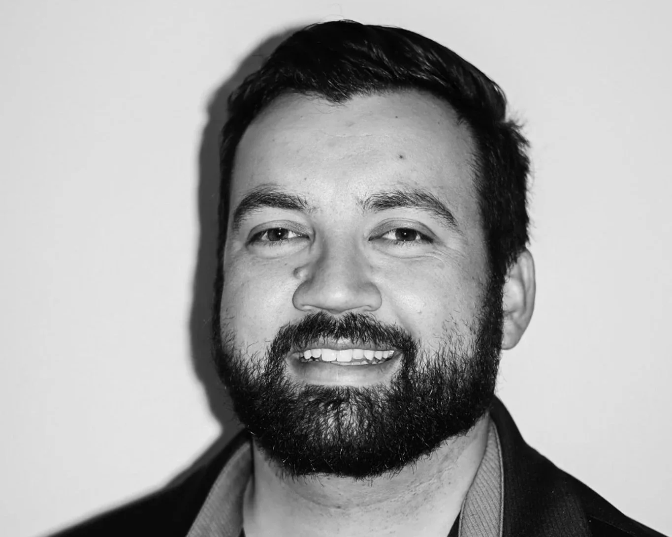 Black and white portrait of a smiling man with a beard and short dark hair, wearing a collared shirt and blazer, facing the camera. A Connect Engineering Employee.