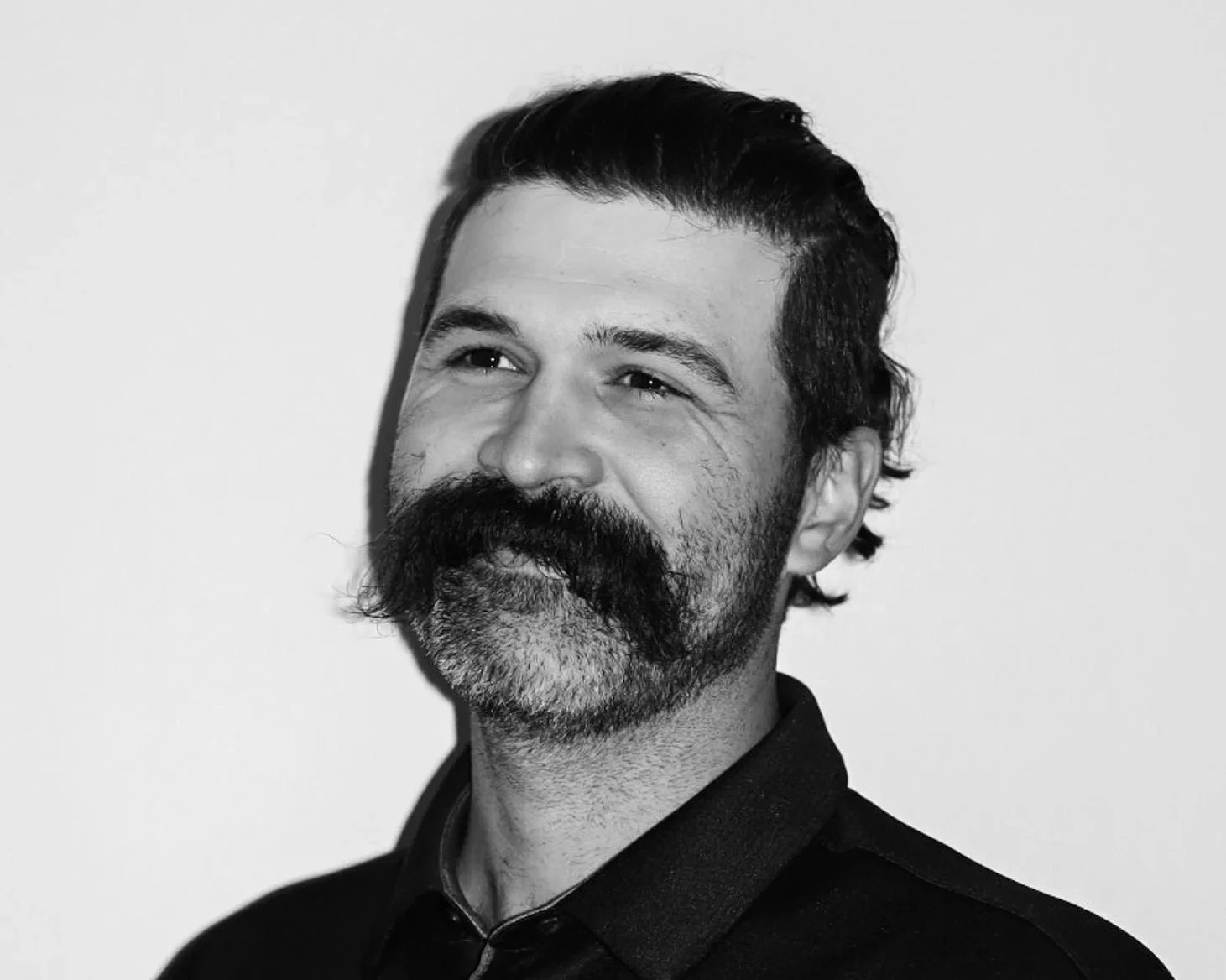 Black and white portrait of a man with a thick mustache and a beard, smiling and looking slightly to the side, wearing a dark shirt. A Connect Engineering Employee.