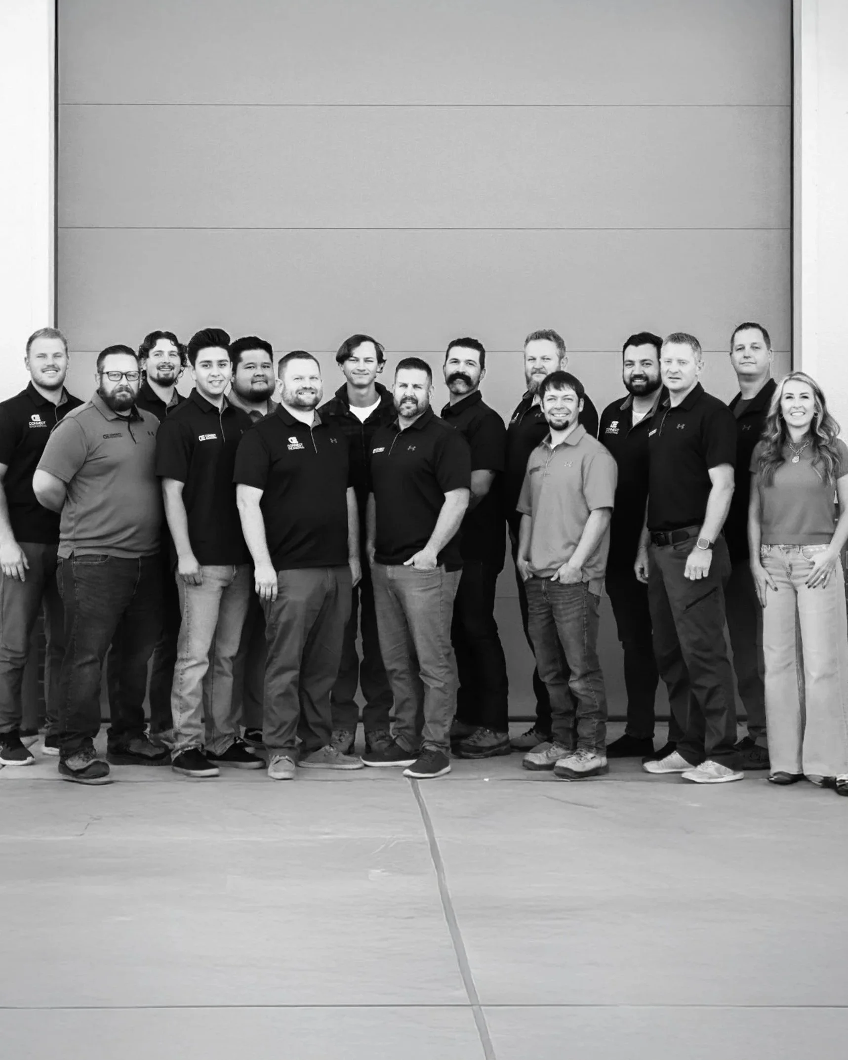 Group of 16 connect engineering employees. people standing in front of a large wall, smiling for the photo. Black and white image.