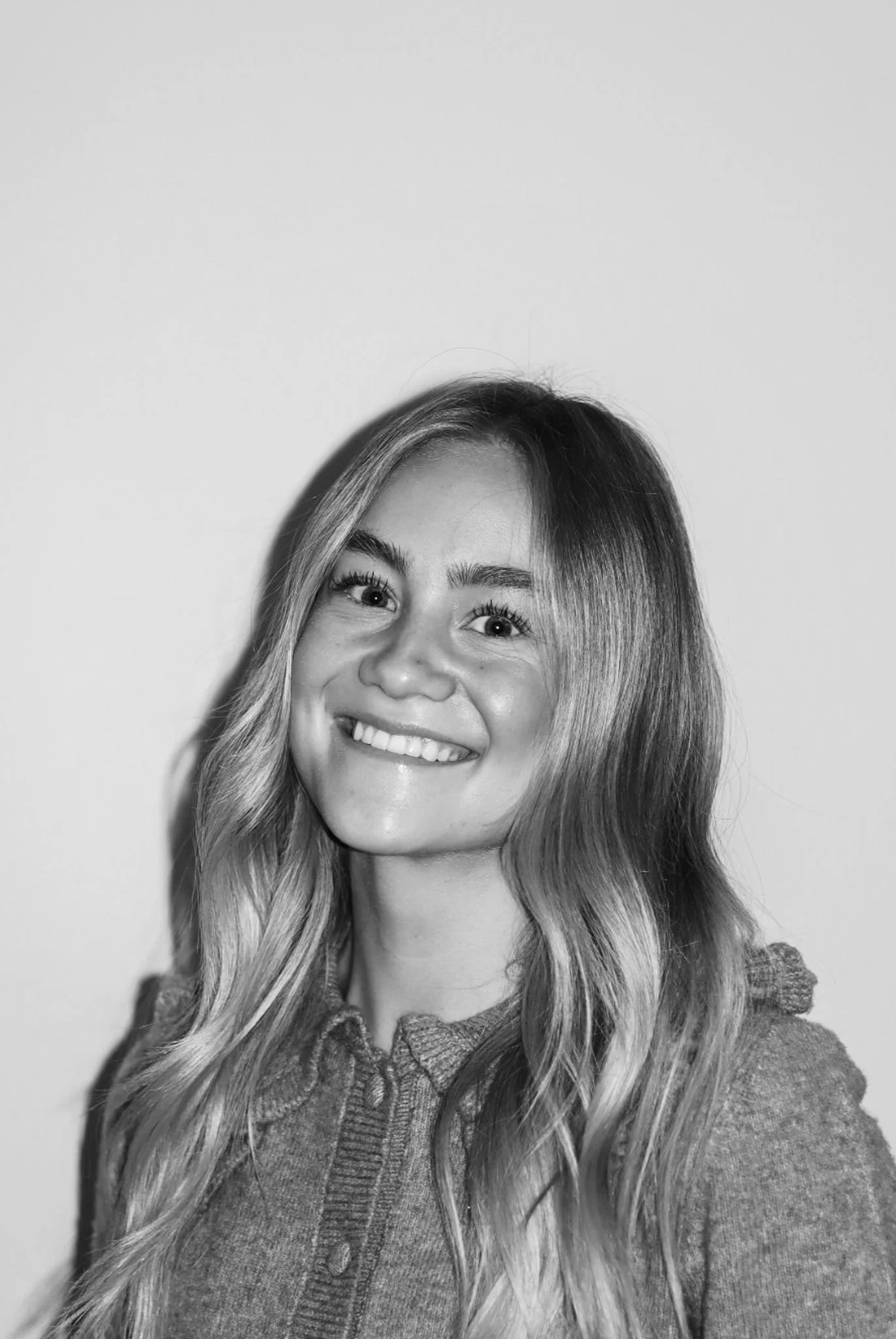 Black and white portrait of a smiling woman with long wavy hair and a textured sweater, standing against a plain background. A Connect Engineering Employee.