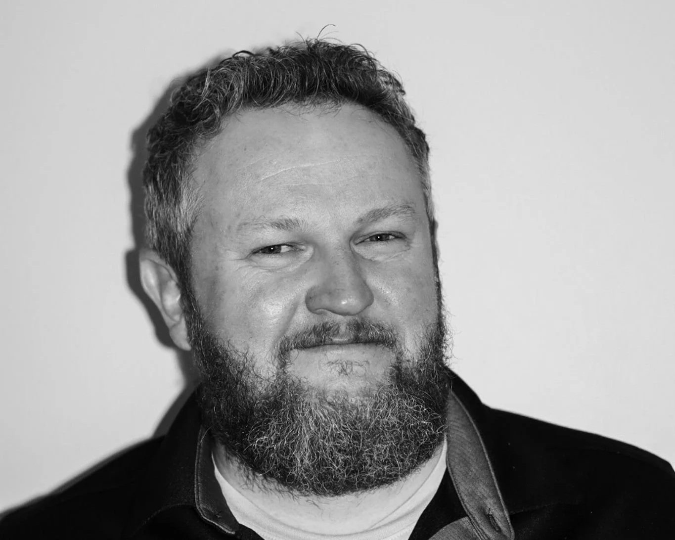 Black and white portrait of a man with a beard and short curly hair, smiling slightly, against a plain background. A Connect Engineering Employee.